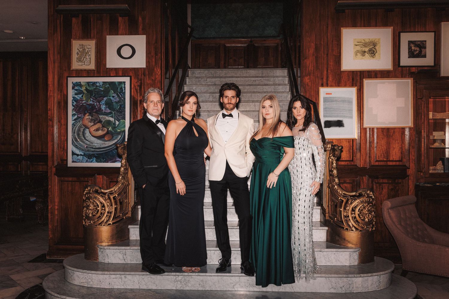 Wedding party posing on elegant staircase with one groom in white tuxedo and guests in formal attire.