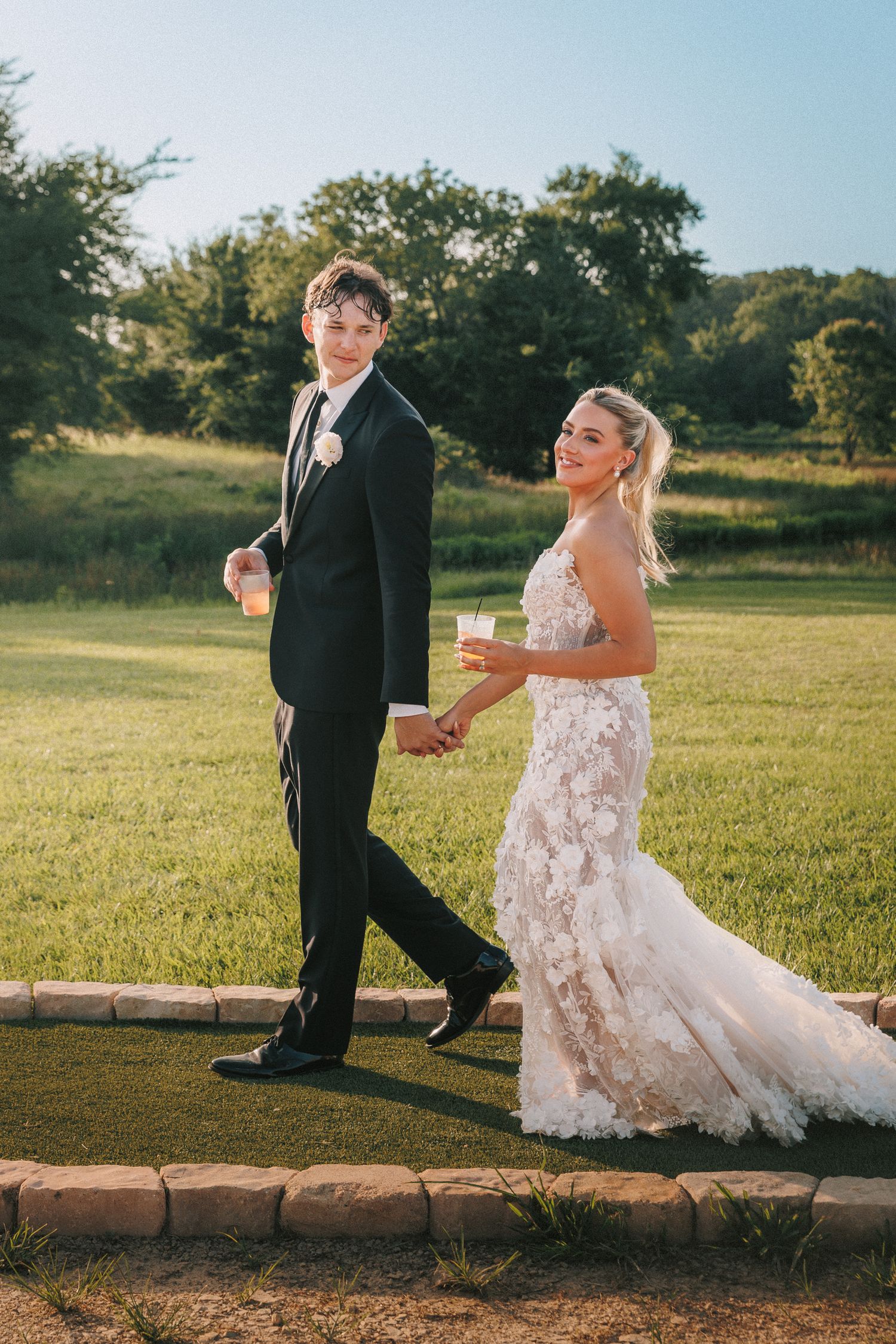 Wedding party members walk along a stone path during an outdoor celebration.