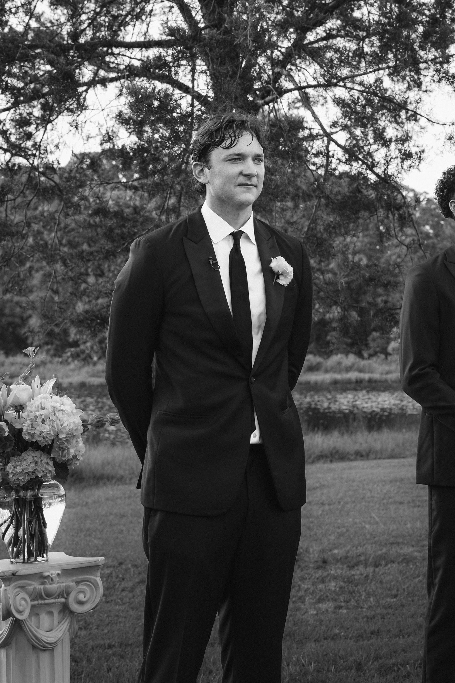 Groomsmen in black suits and ties stand together outdoors in a black and white photograph.