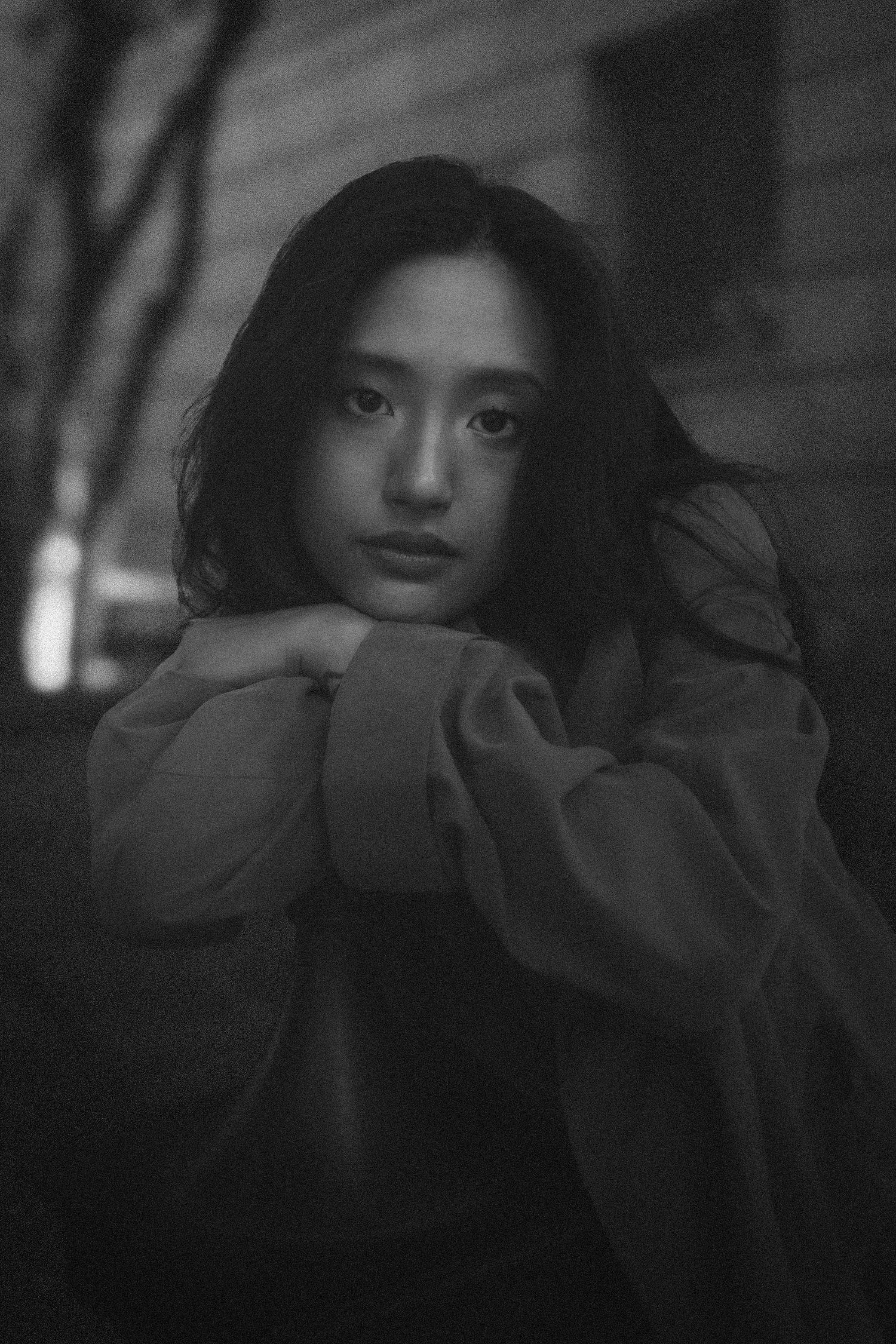 A black and white artistic portrait showing someone in contemplative pose against a dark background.