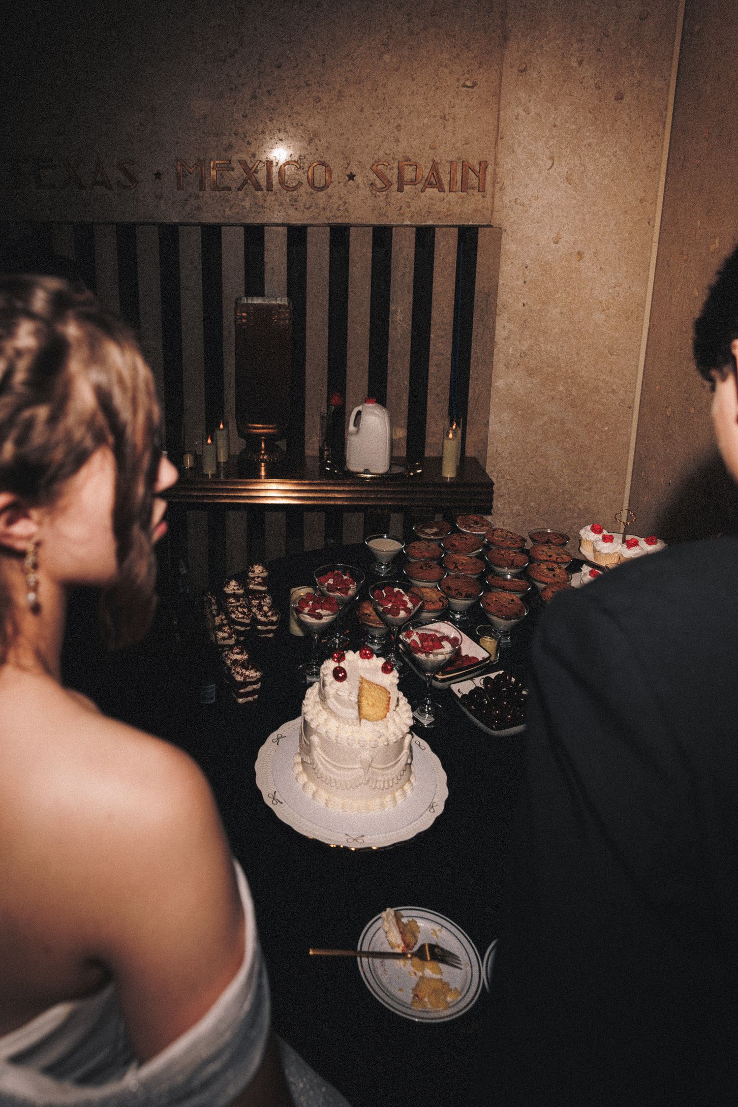 Bride and groom view wedding cake and dessert table beneath Texas Mexico Spain sign at reception.