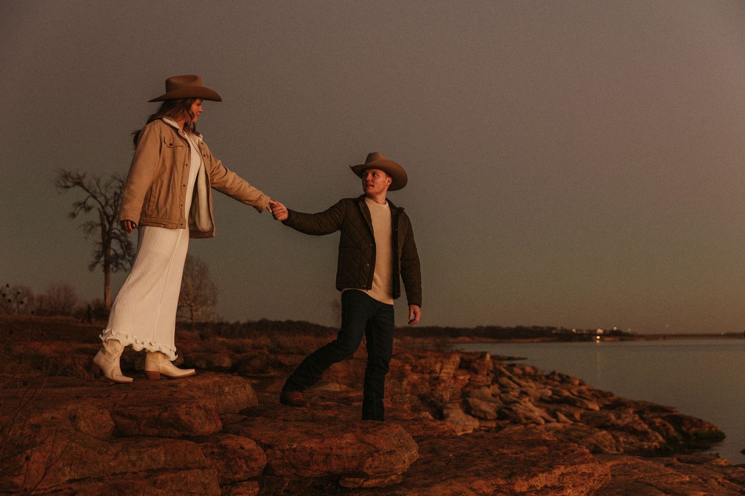 Silhouettes of couple in western attire dancing together on rocky terrain at dusk.