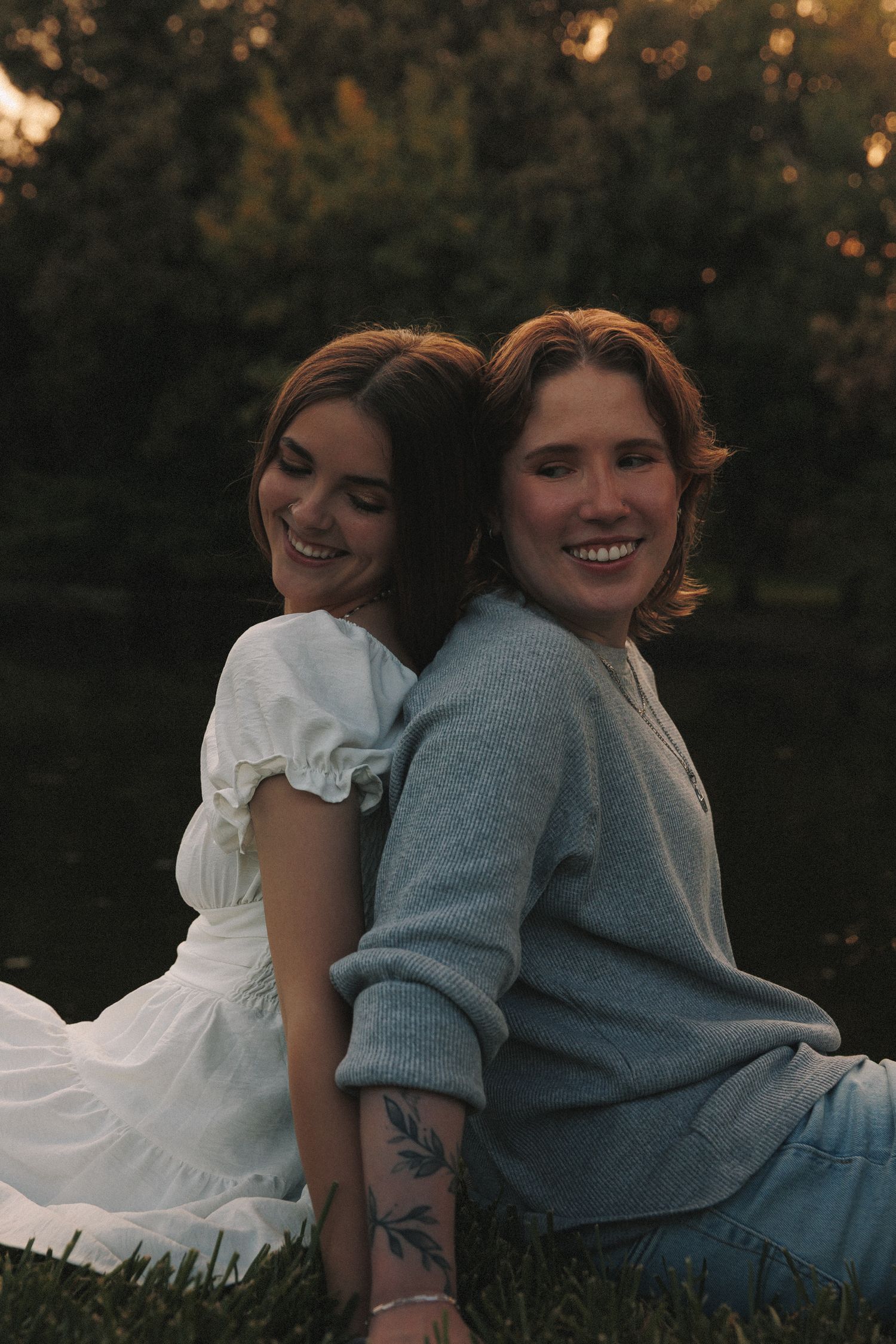 Two people in casual attire share a tender moment while sitting together on grass during golden hour.