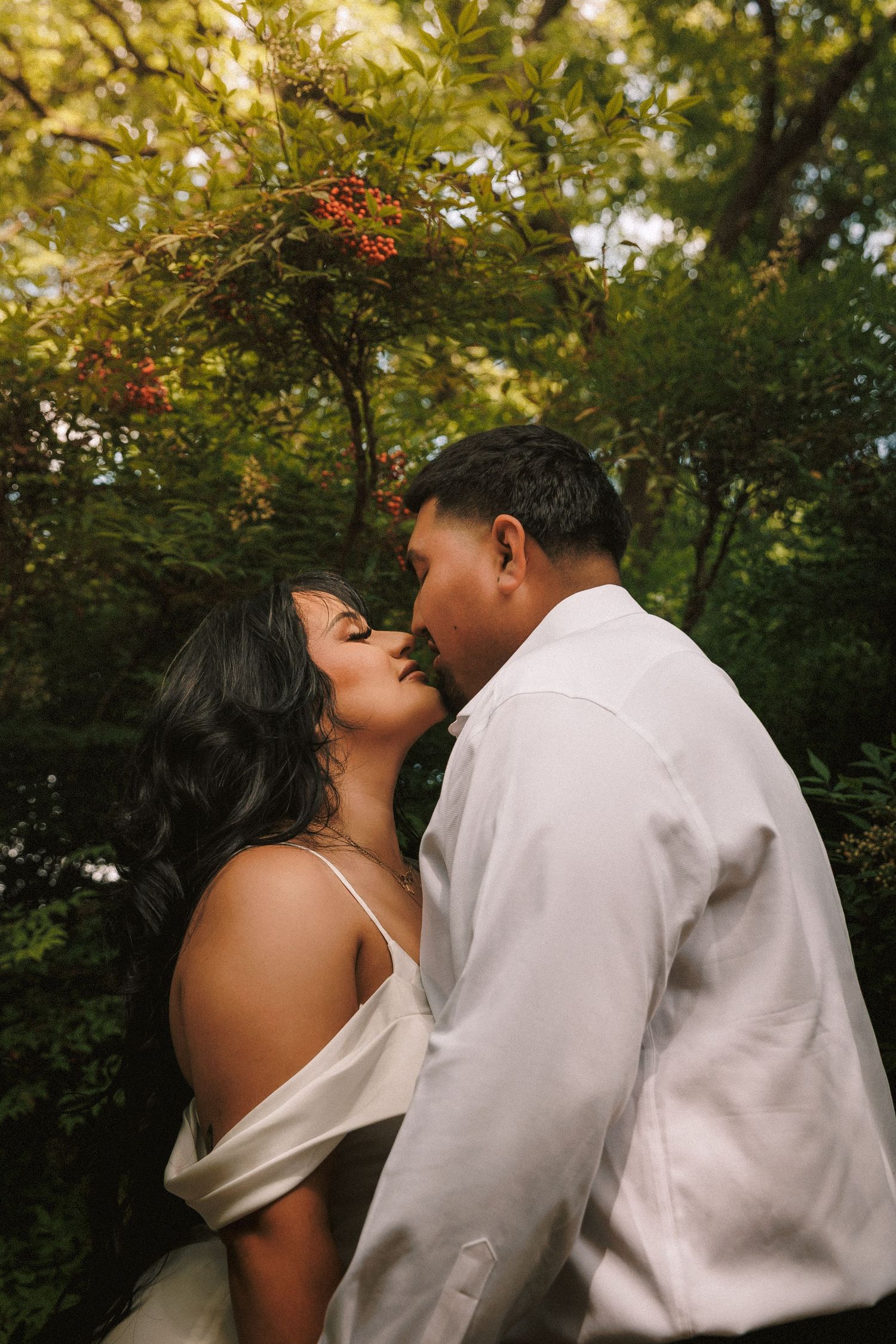 A romantic moment between a couple embracing in an intimate outdoor setting with lush green trees in the background.