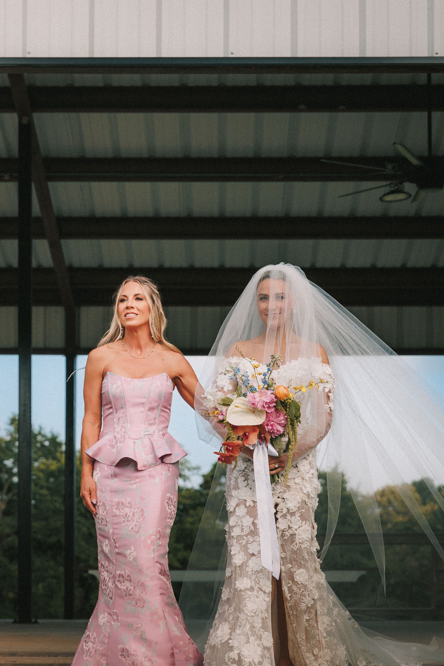 Wedding party in pink and white dresses poses beneath industrial ceiling.