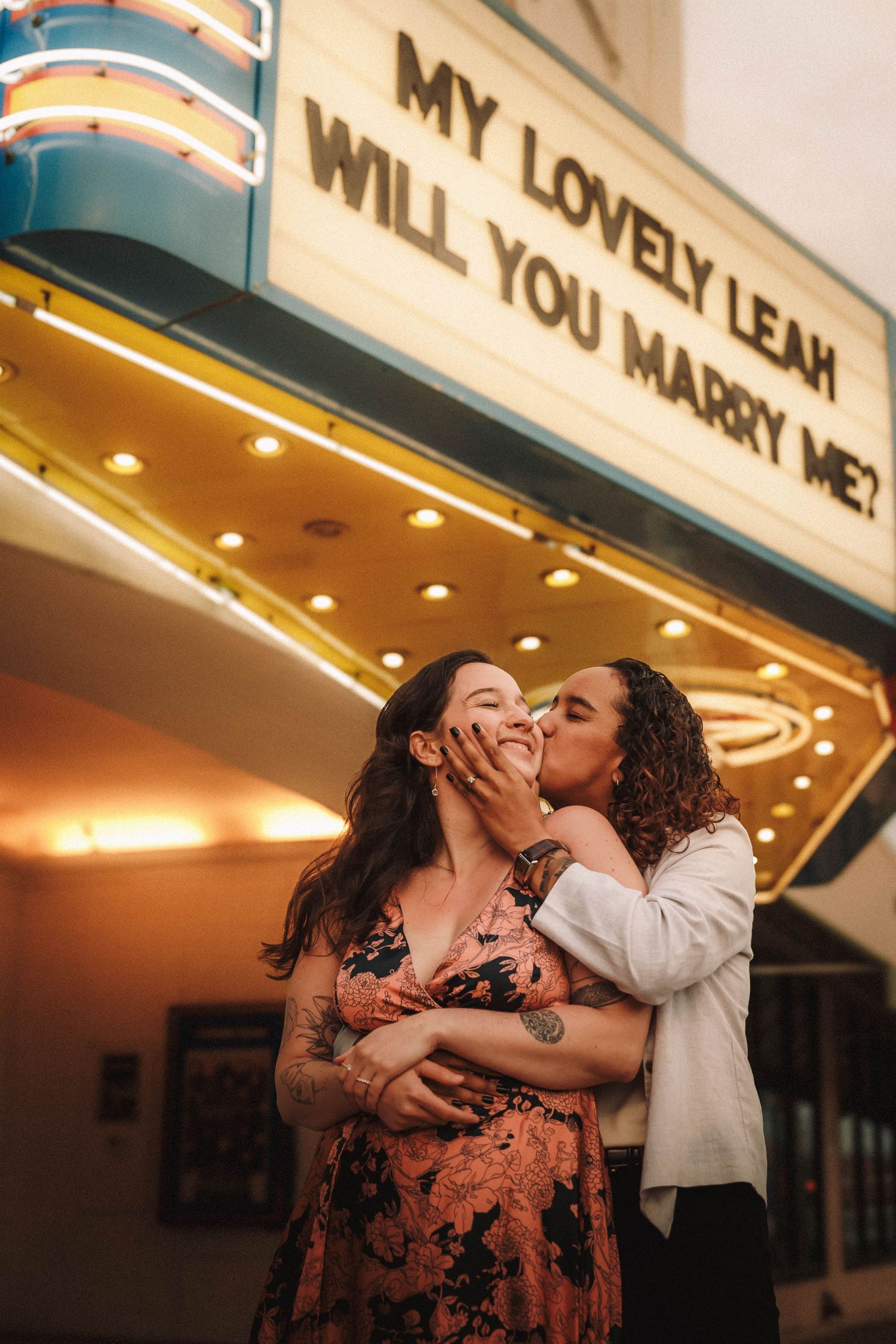 A romantic proposal moment under illuminated theater marquee lights with confetti flying through the air.