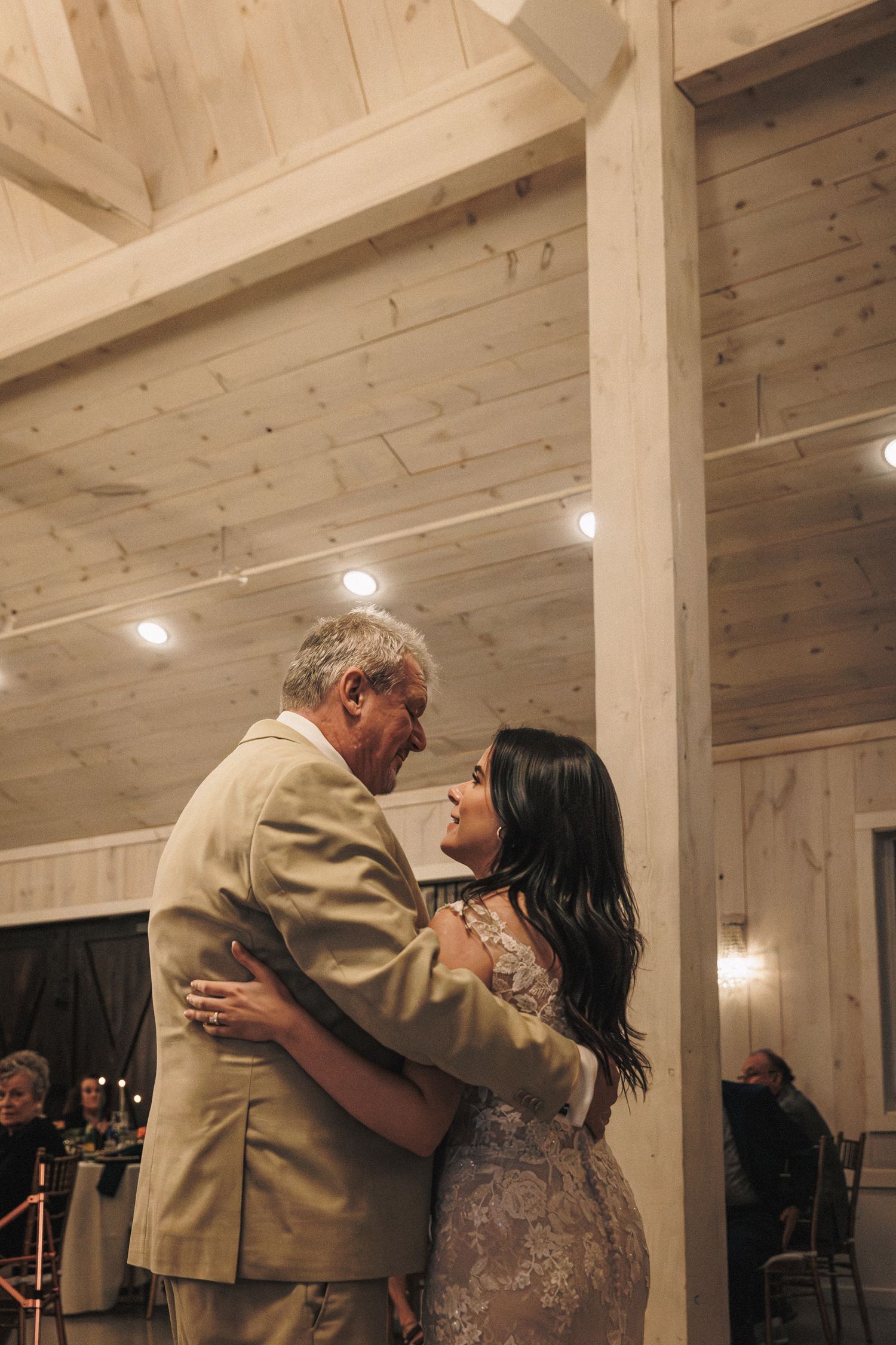 Bride and her father share an emotional father-daughter dance in a rustic wood-paneled wedding venue.