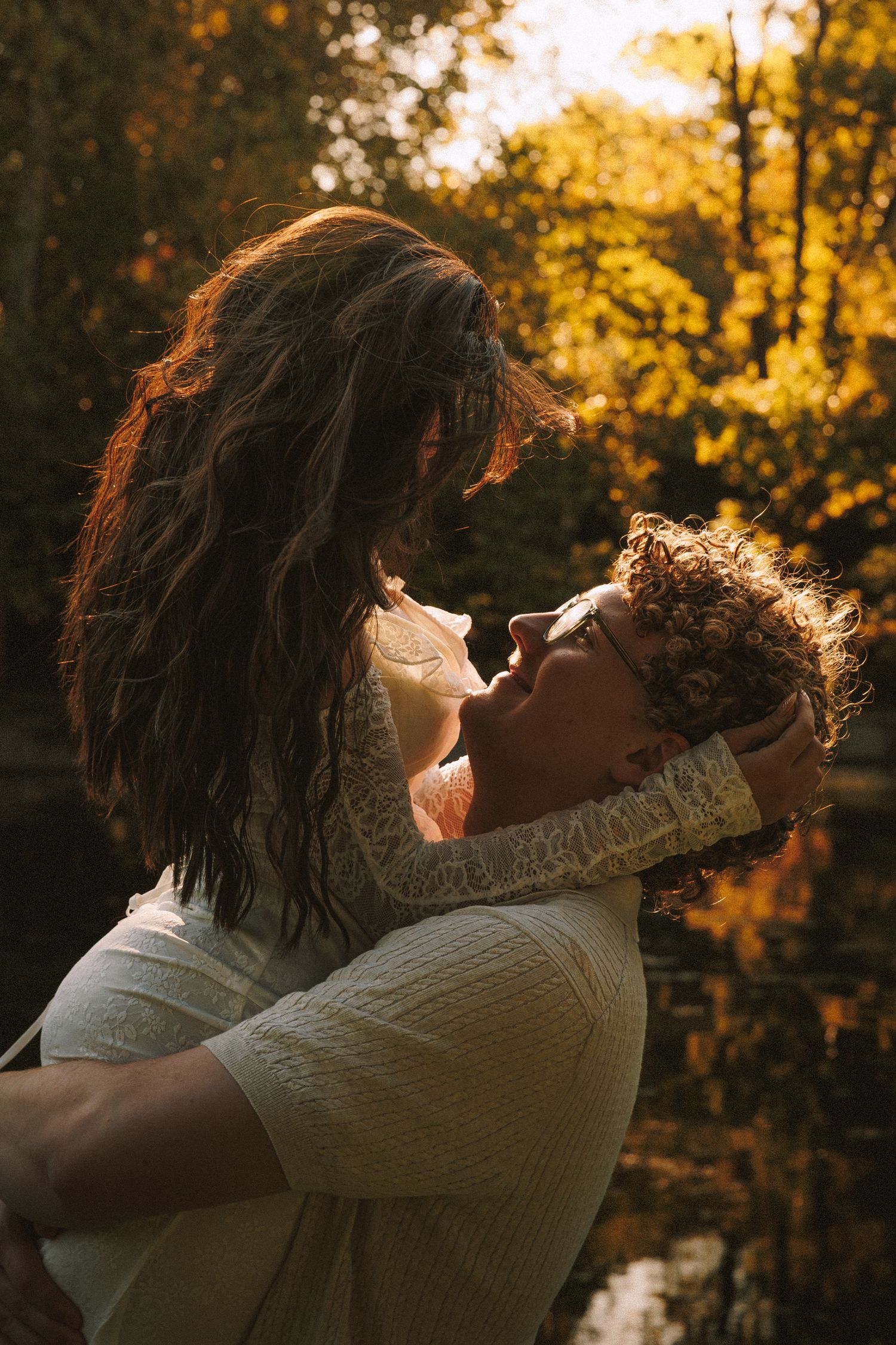 A couple embraces in a romantic dance pose against a golden sunset through autumn trees.