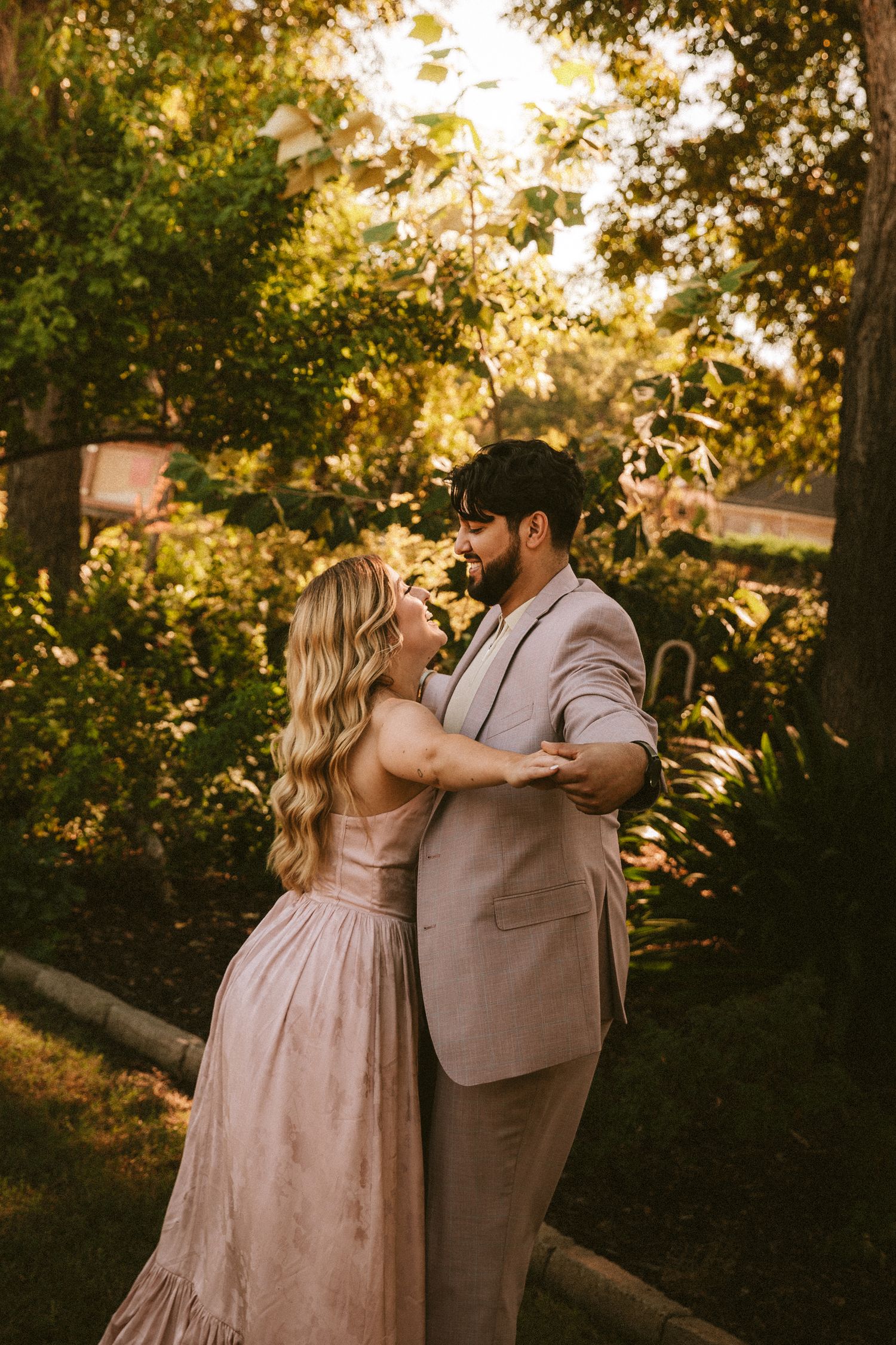 A couple in coordinating blush tones sharing a romantic dance in a garden during sunset.