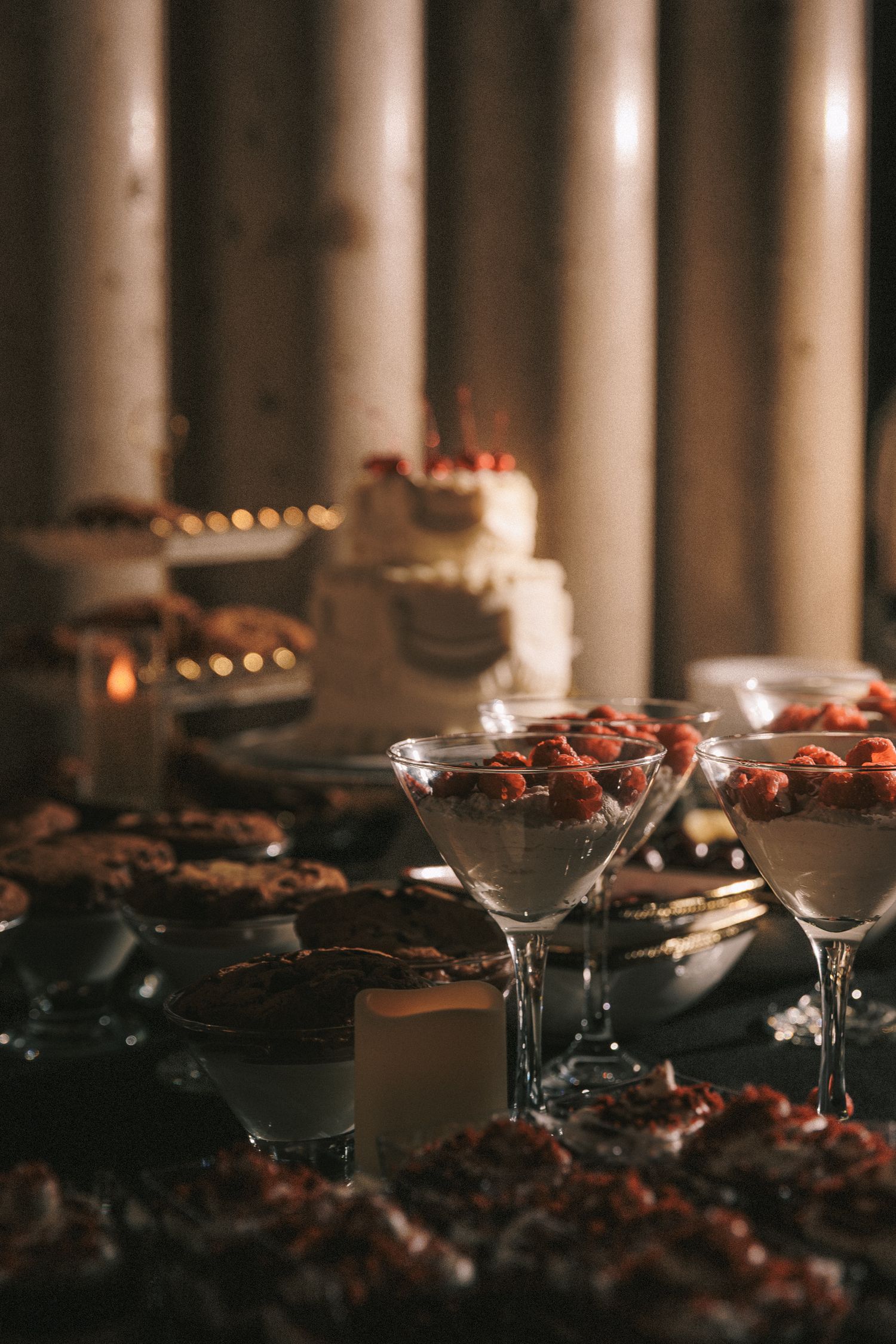 Wedding dessert table featuring strawberry parfaits in martini glasses, cookies, and white tiered cake.