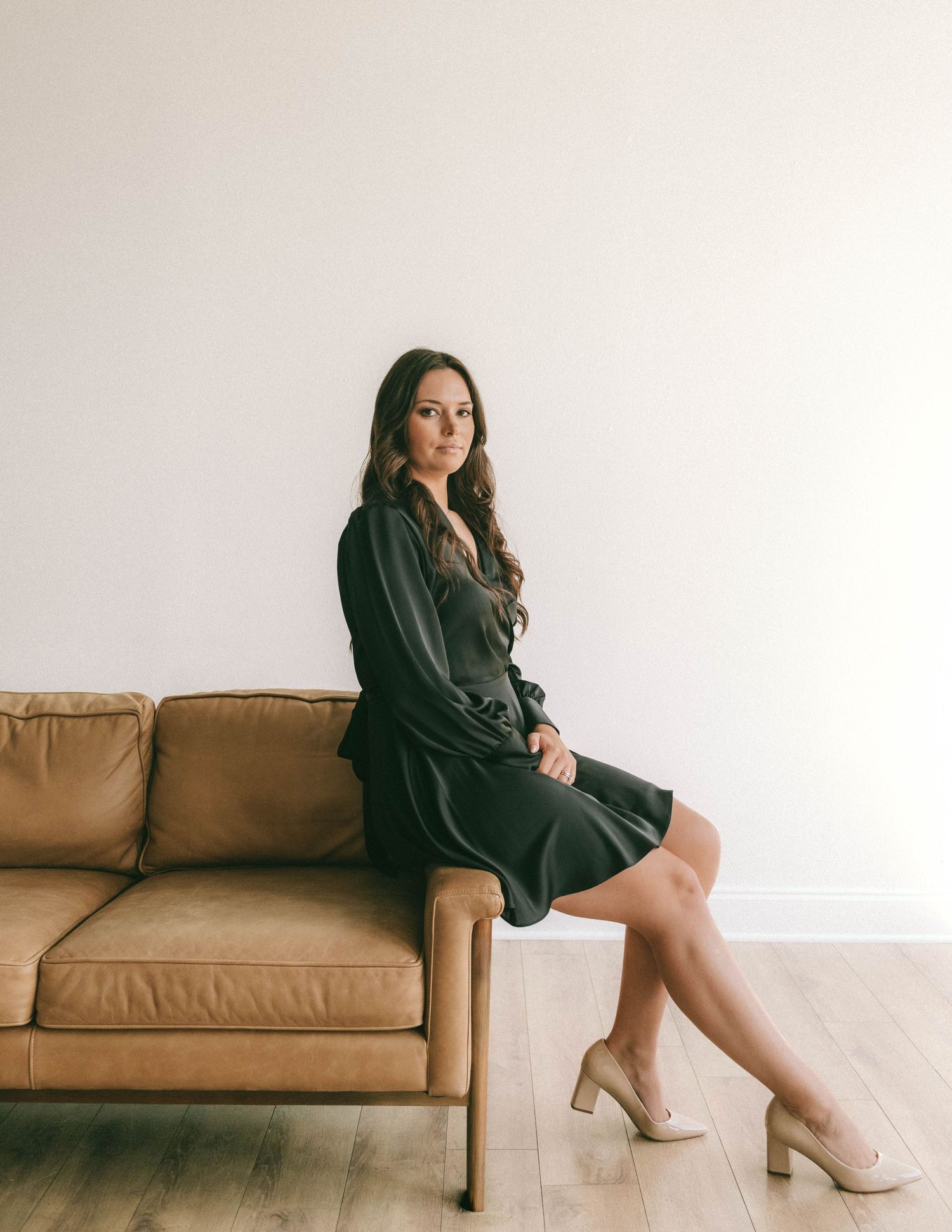 Lifestyle photo series showing someone in black loungewear posed casually on a tan leather sofa against white walls.