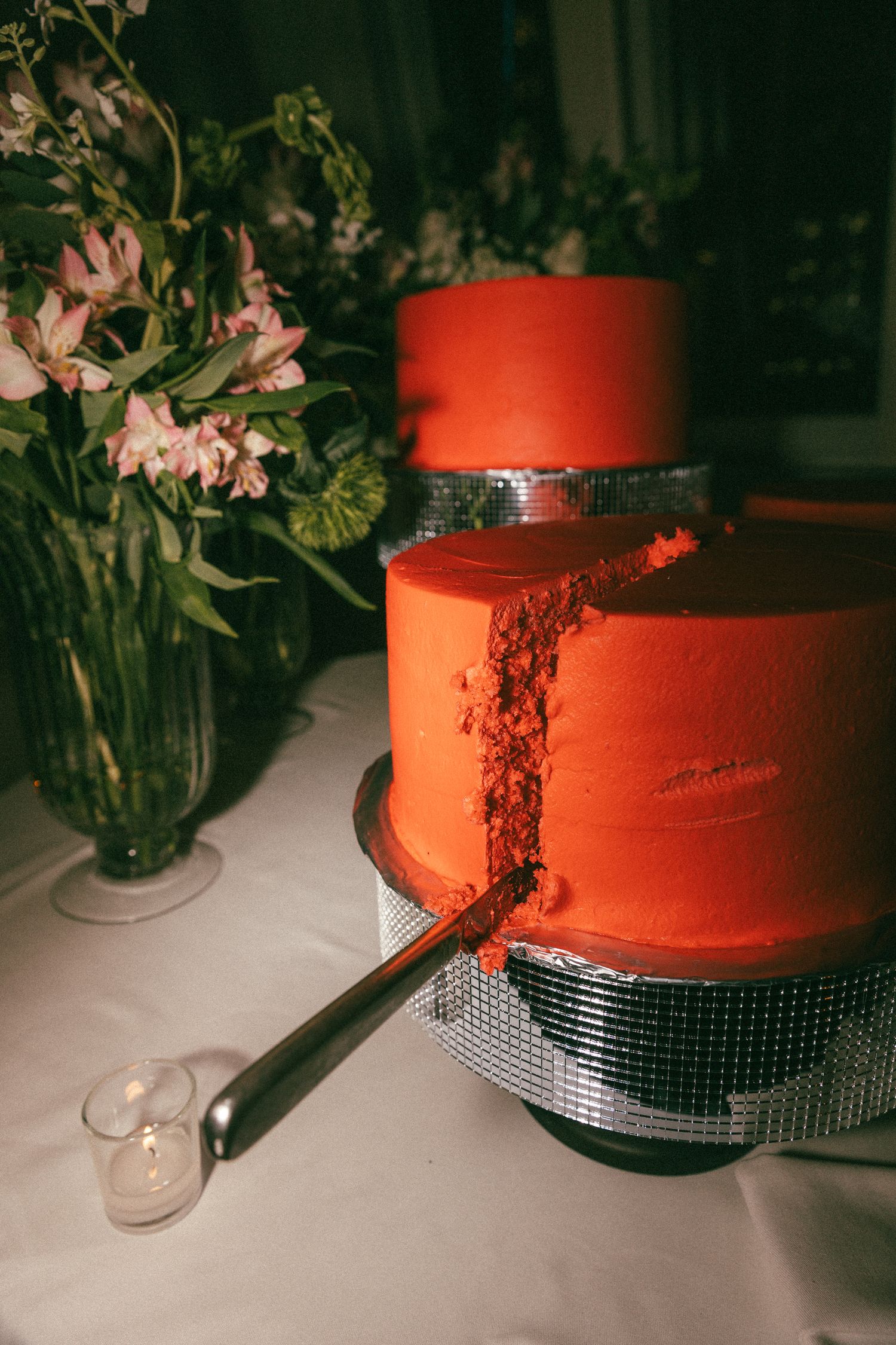 Two-tier red wedding cake with silver disco ball base beside a floral arrangement.