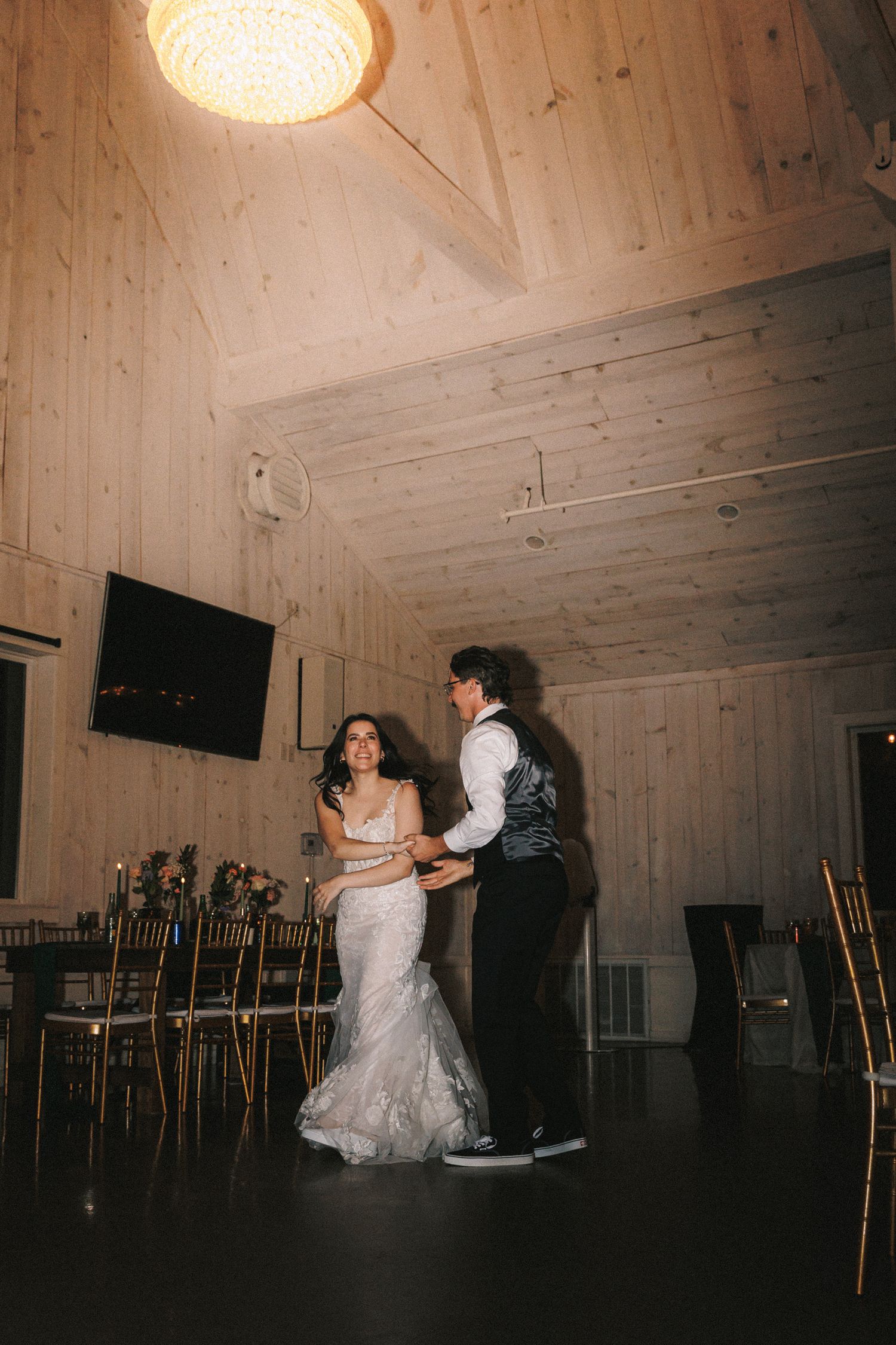 Bride and groom share their first dance in a warmly lit rustic wood-paneled venue.
