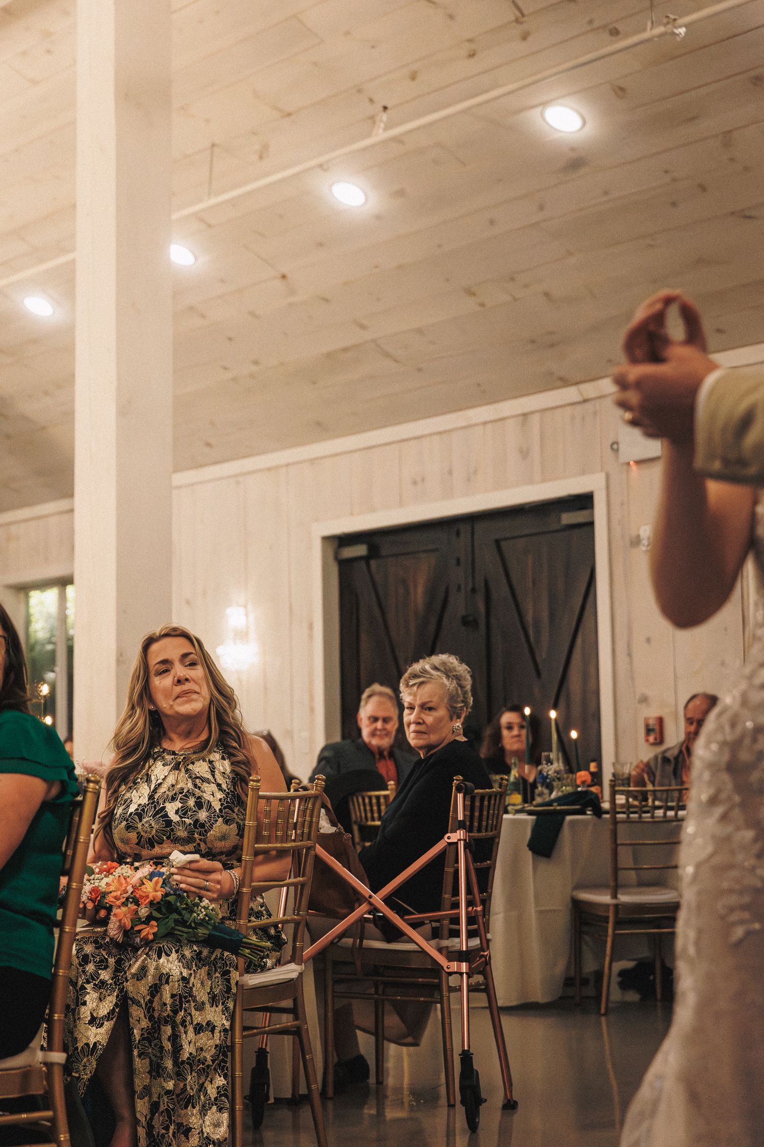 Wedding guests watching bouquet toss in a white barn reception venue with dark doors.