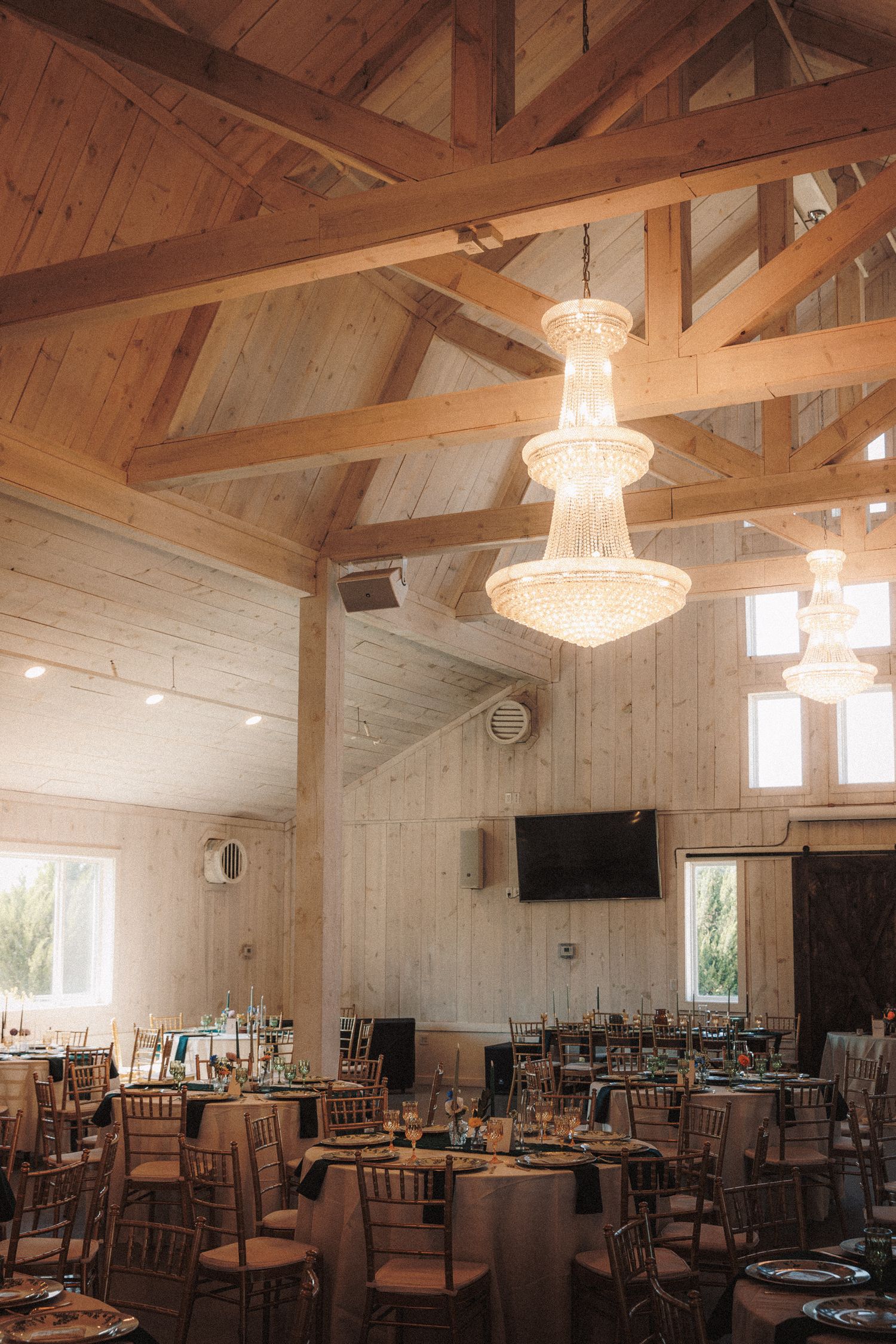 Rustic barn wedding reception hall with crystal chandeliers and round tables set for dining.