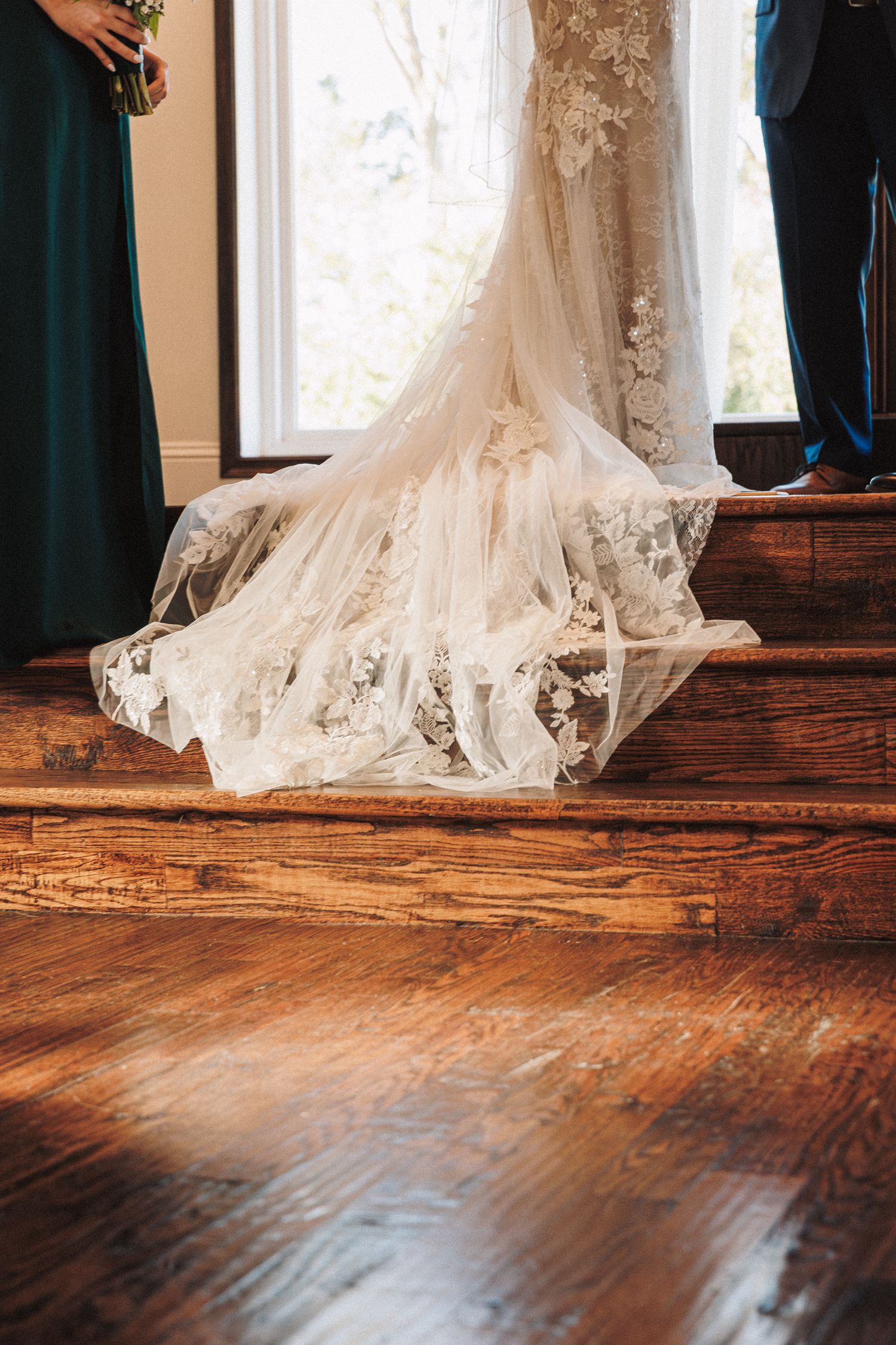 Elegant lace wedding dress train spreads across rustic wooden church steps.