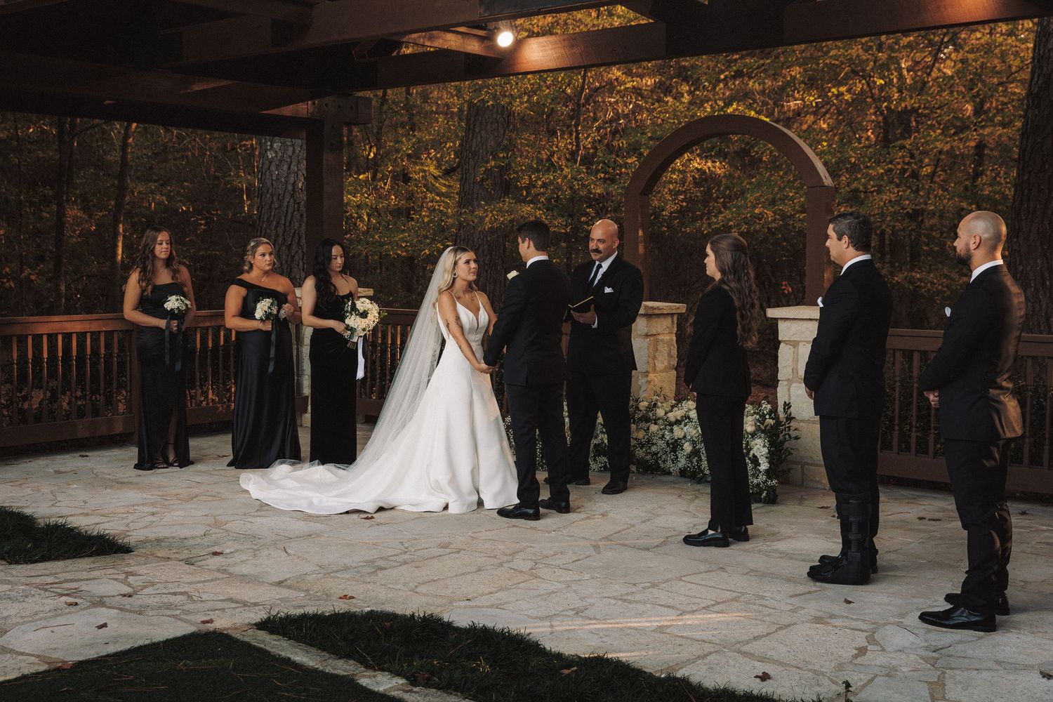 Bride and groom exchanging vows at outdoor wedding ceremony with wedding party.