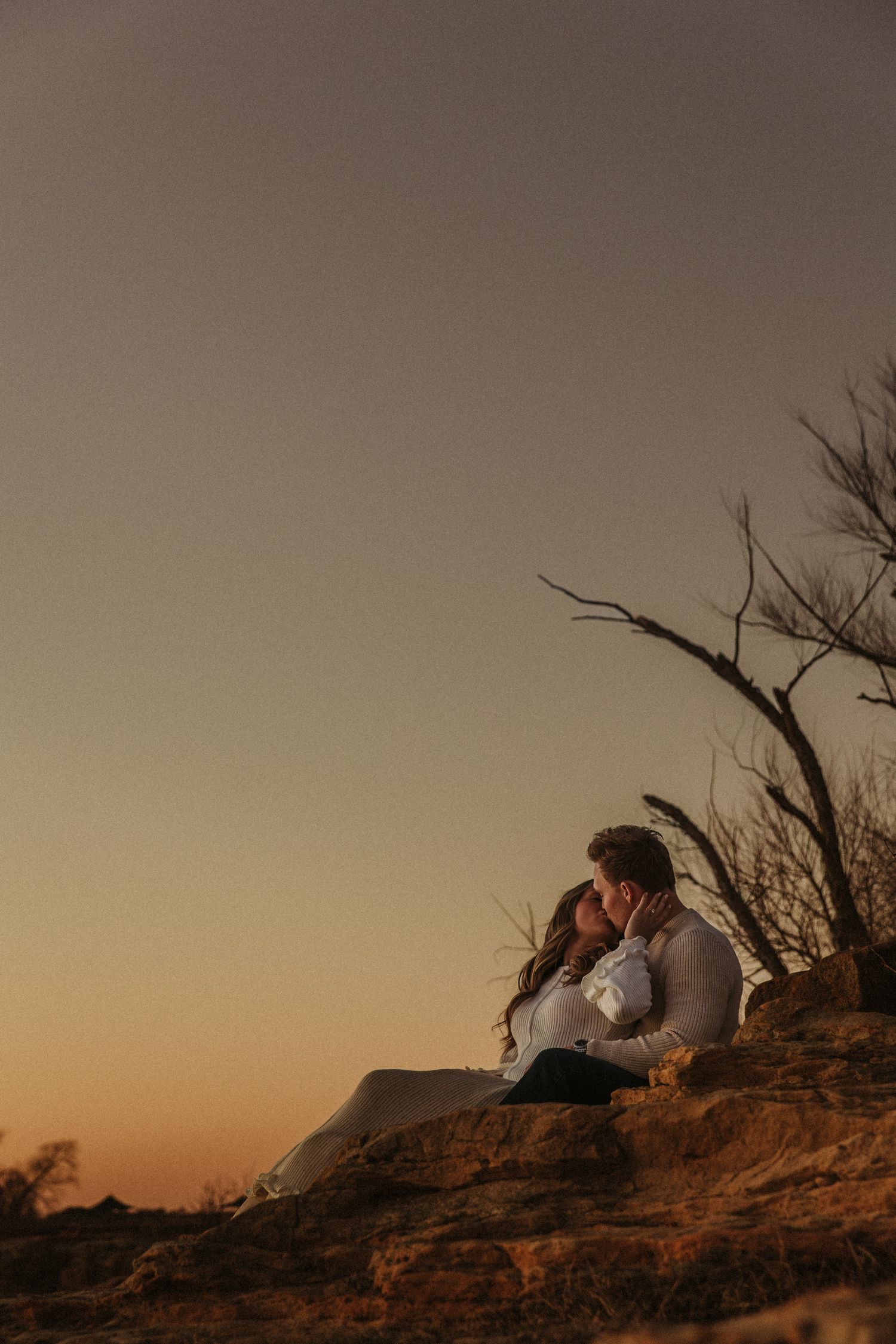 Couple sitting together on rocky cliff edge during golden hour sunset.