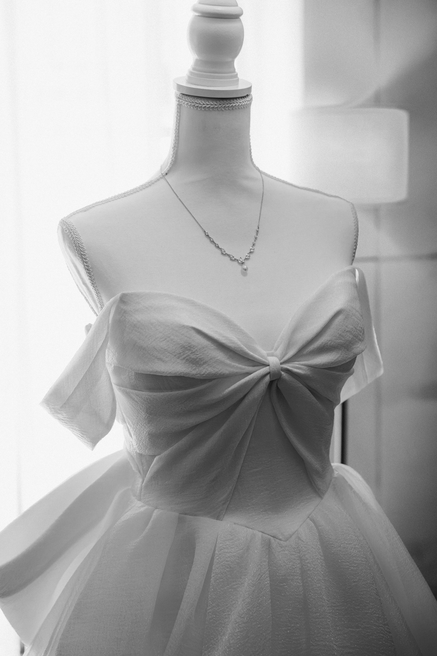 White strapless wedding gown with bow detail on mannequin with delicate diamond necklace, black and white.