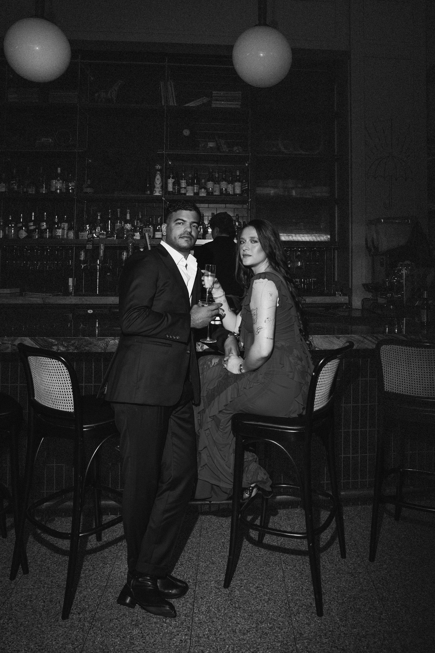 Elegant couple posing at a bar with cocktails in black and white photography.
