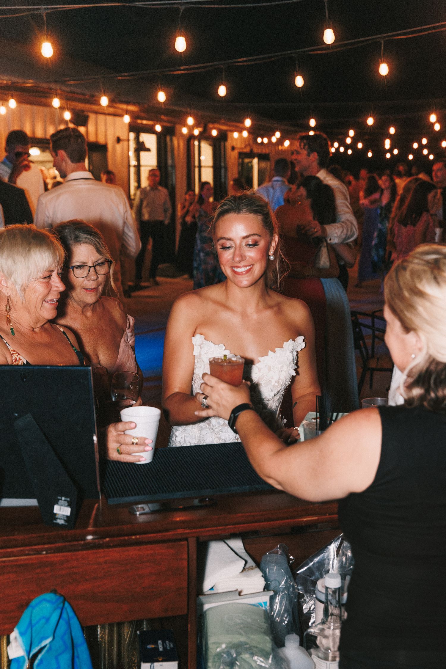 Wedding reception guests dance and celebrate under hanging string lights at an evening outdoor venue.