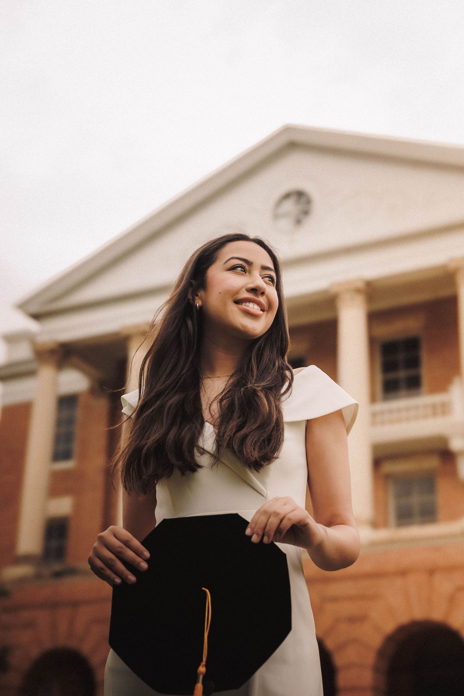 Student celebrates graduation in black and white attire while spinning playfully near collegiate building.