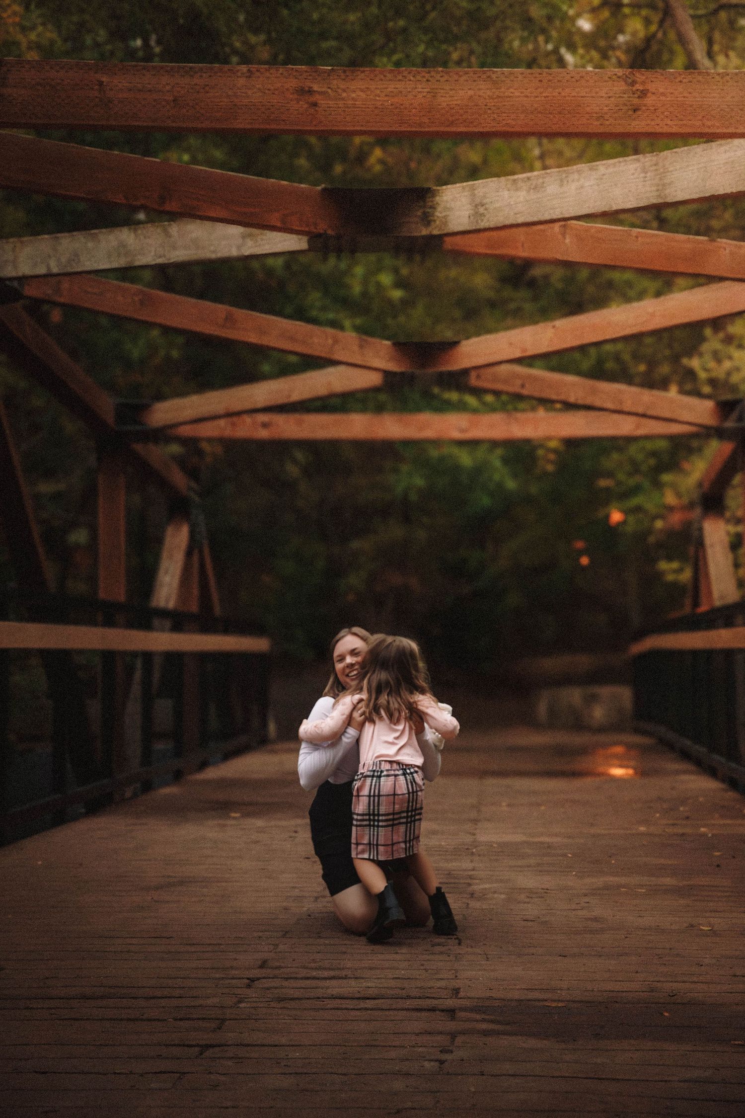 Two figures sitting on a rustic wooden bridge at sunset with warm autumn lighting filtering through the trees.