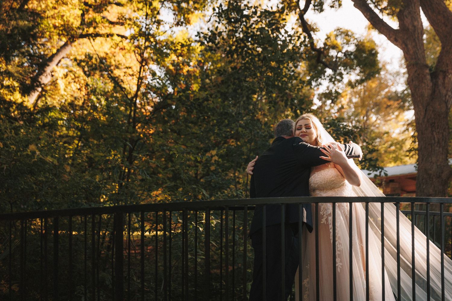 Bride and groom sharing romantic embrace on garden balcony surrounded by autumn foliage.