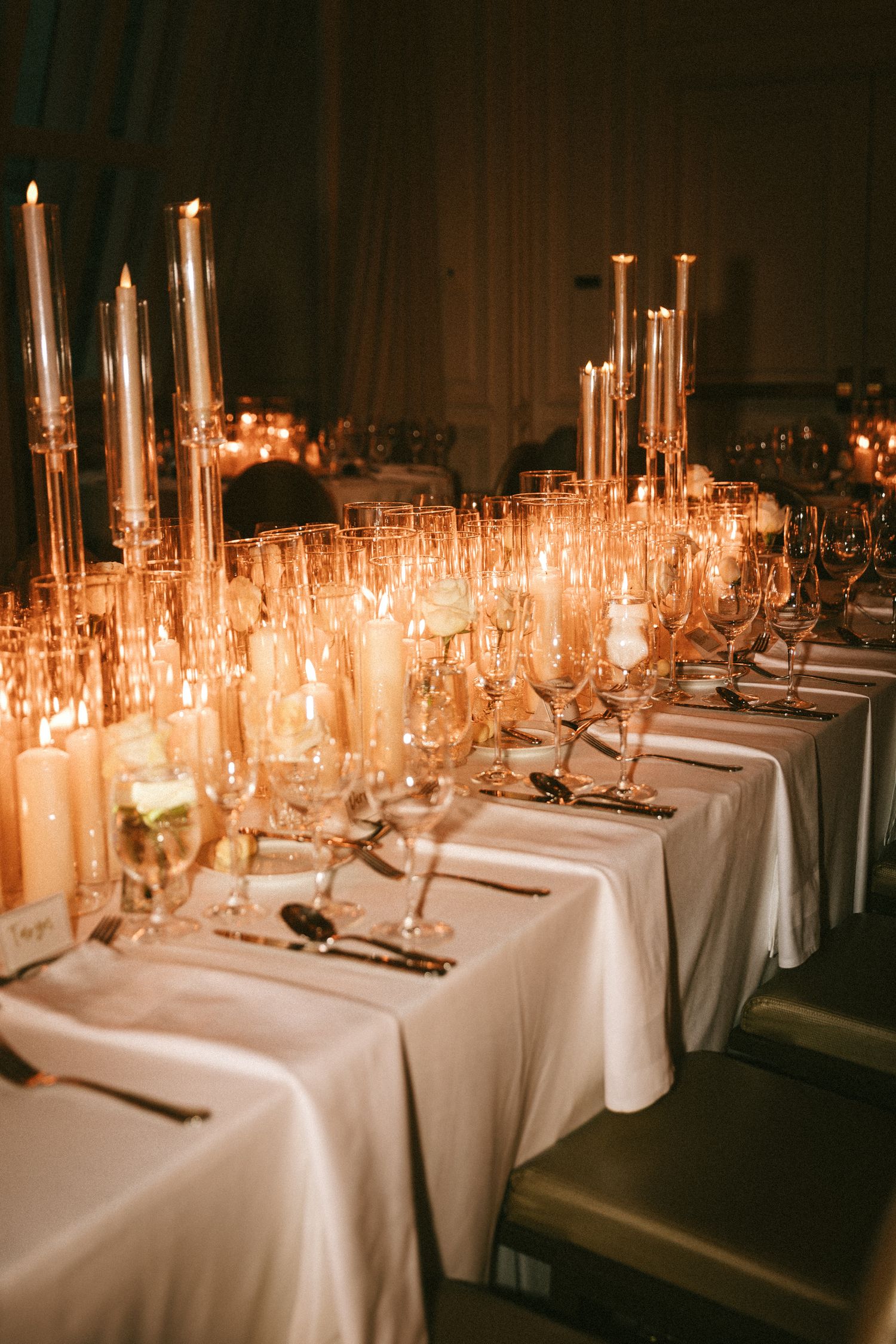 Elegant wedding reception table set with tall candles, crystal glasses, and white linens.