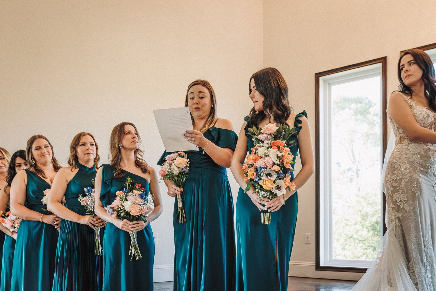 Bridesmaids in teal dresses hold bouquets during a wedding ceremony reading.