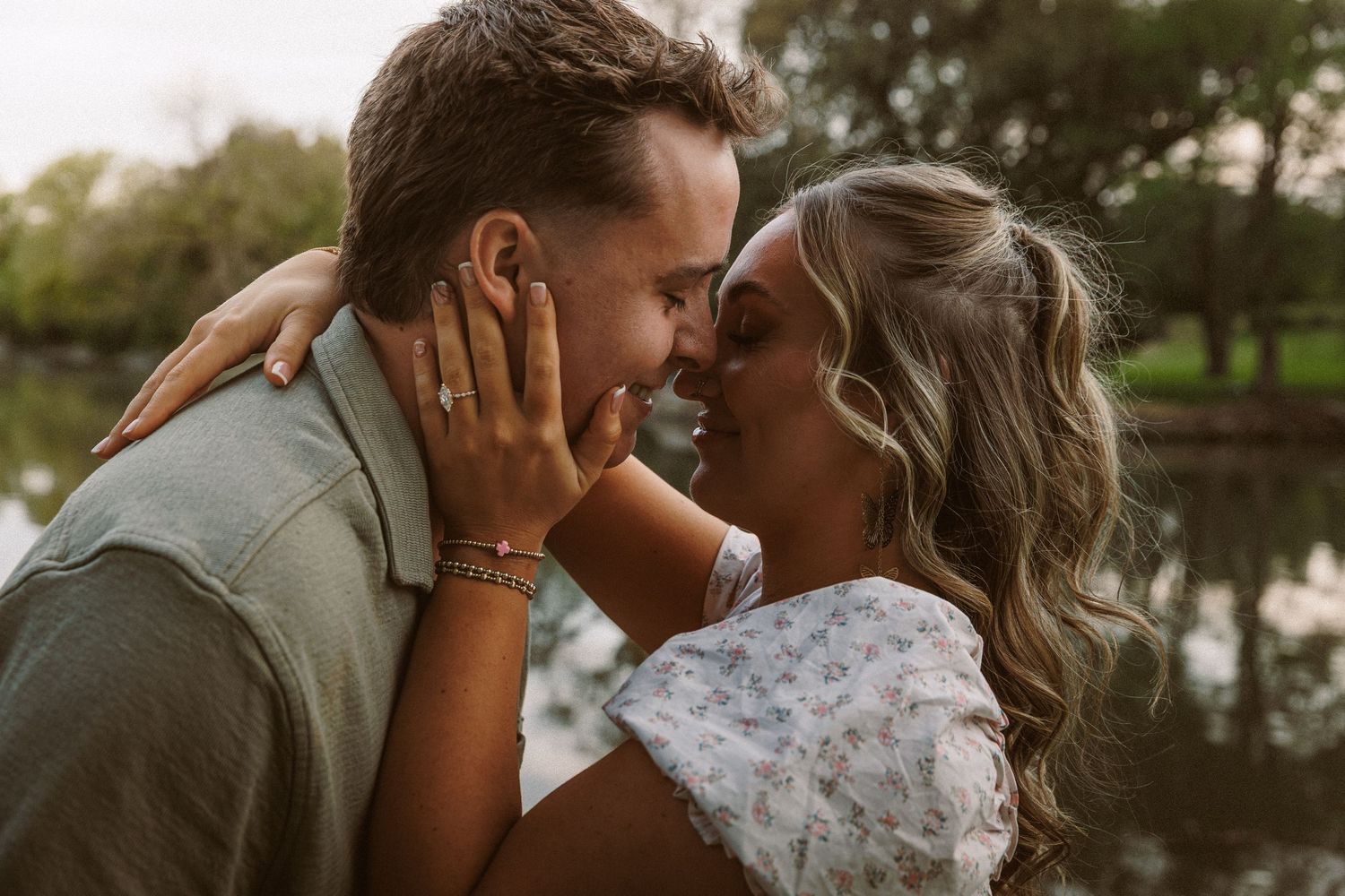 Couple sharing a romantic moment about to kiss near a serene pond at golden hour.