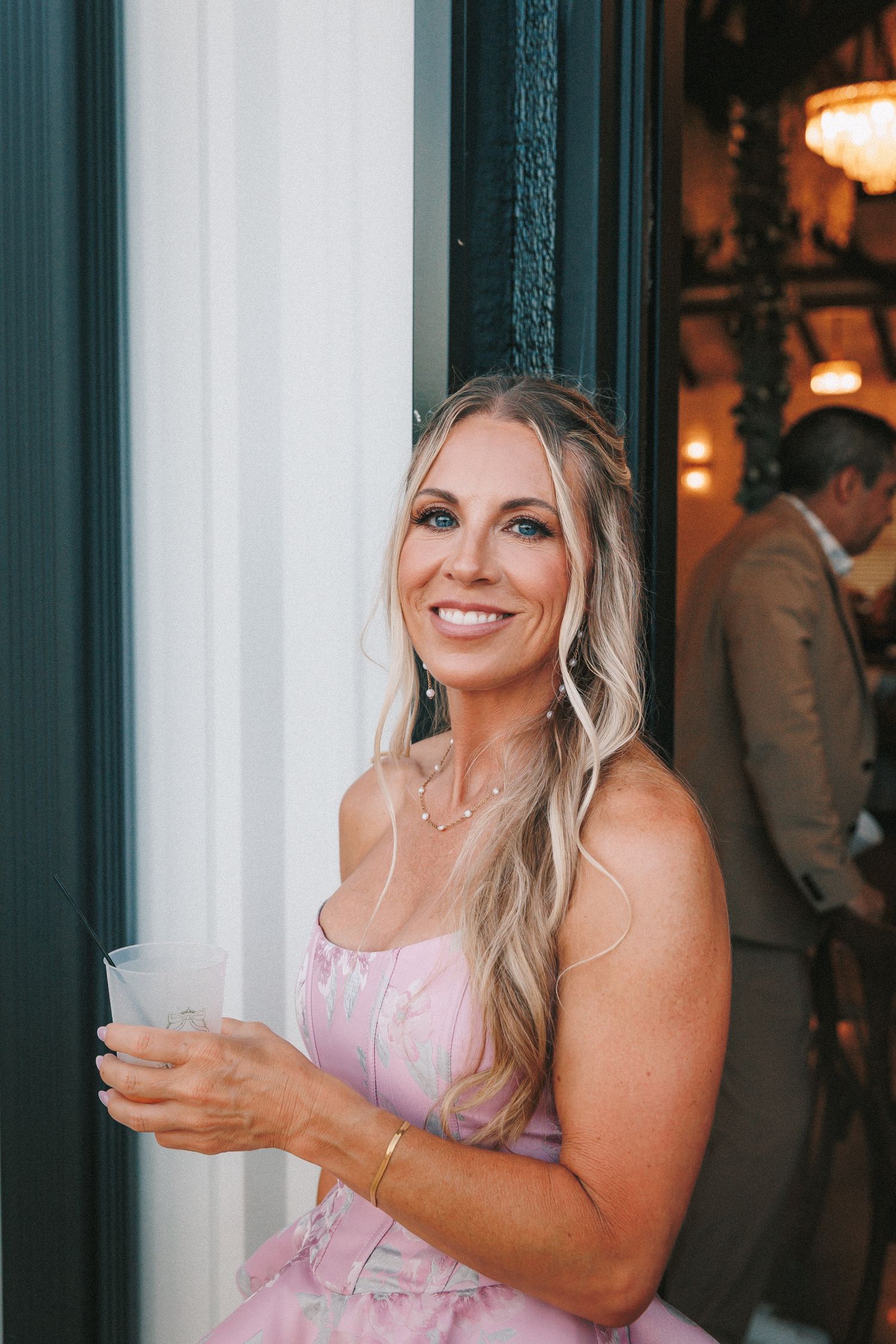 Guest in pink dress enjoying reception festivities near a dark-framed window.