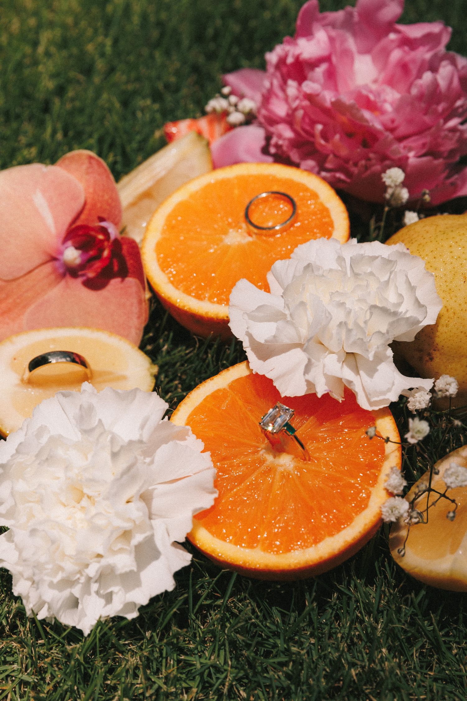 Fresh cut flowers and orange slices arranged on green grass creating a vibrant spring composition.
