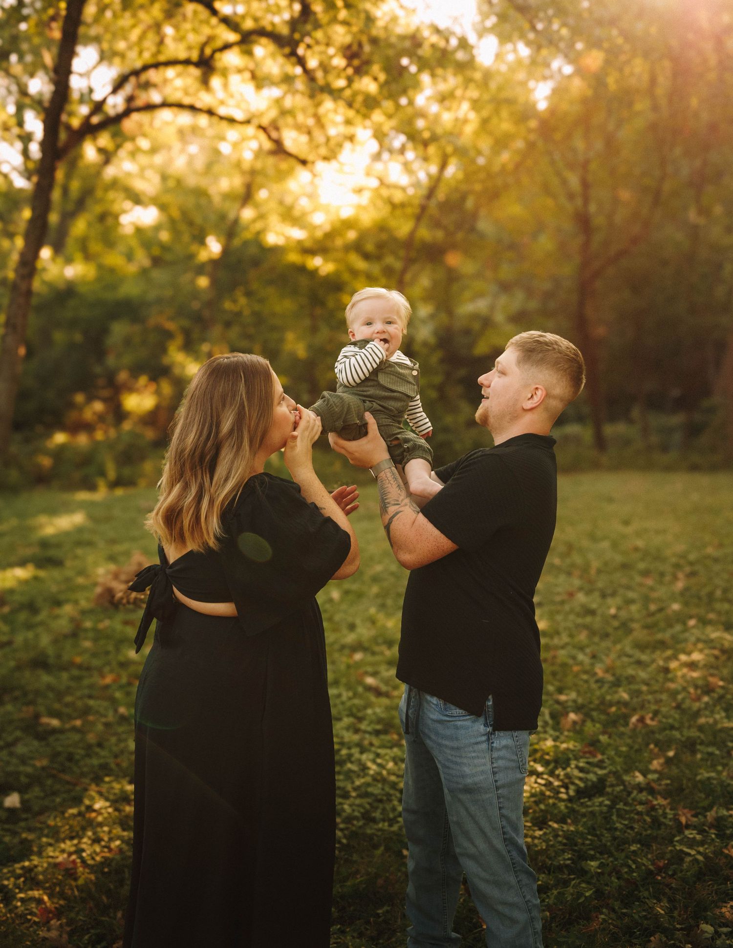 Family having a tender moment together in a park during golden hour with autumn trees and fallen leaves in background.