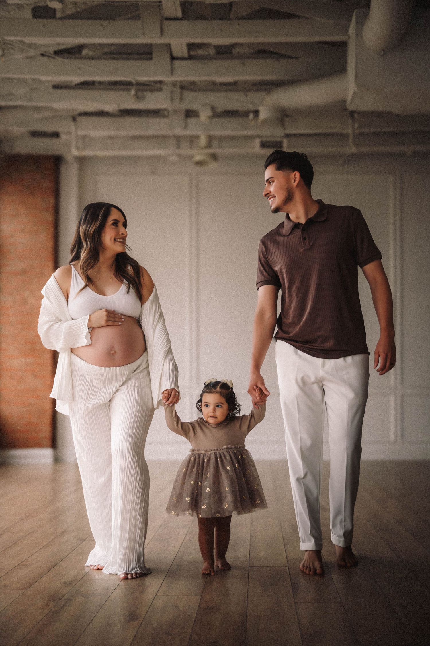 A family walking together barefoot across a wooden floor in coordinated white and brown outfits.