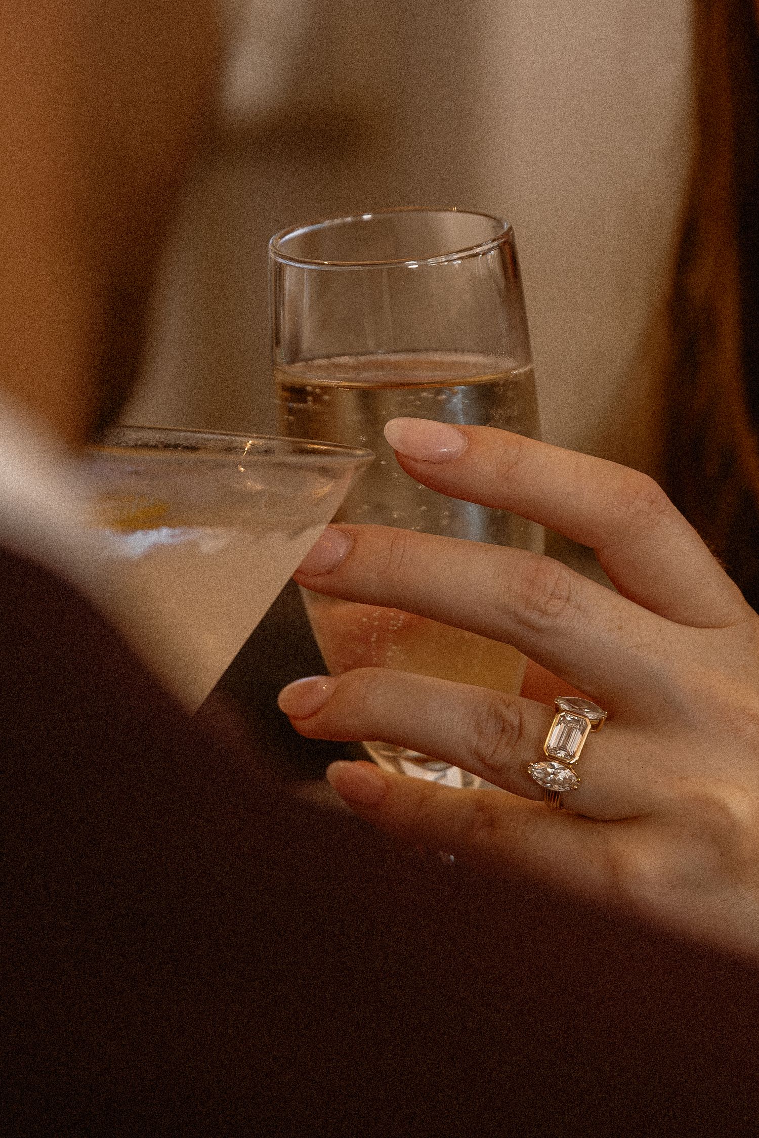 Close-up of a hand holding a glass of champagne, adorned with an elegant emerald-cut diamond ring.