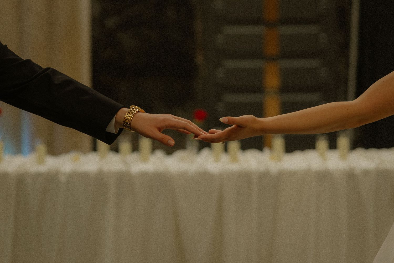 Close-up of bride and groom gently holding hands over a candlelit reception table at wedding.