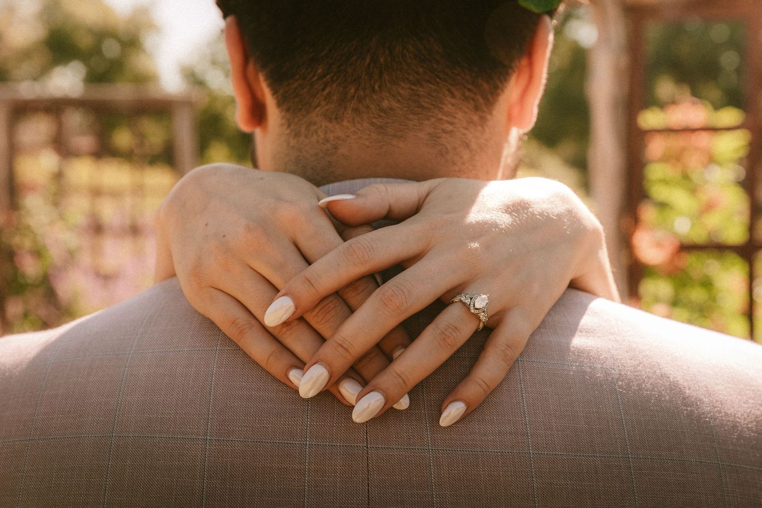 Close-up shot of hands gently resting on shoulders in warm sunlight.