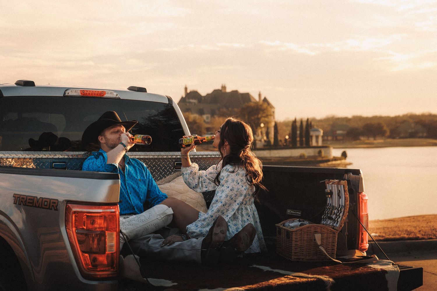 Two people sitting in the back of a pickup truck enjoying a sunset by the water.