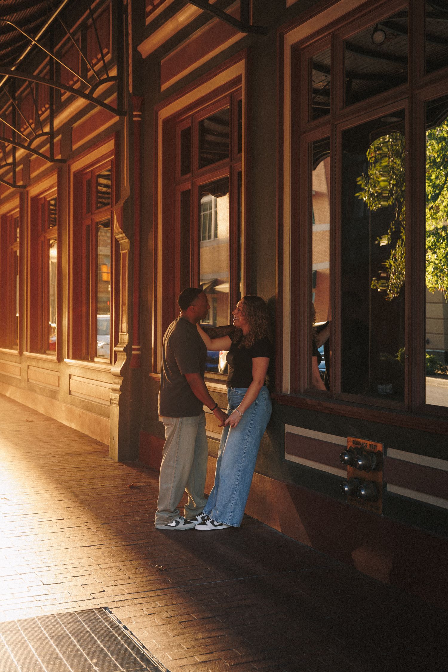 Couple looking through storefront windows along a covered walkway at dusk with warm lighting.