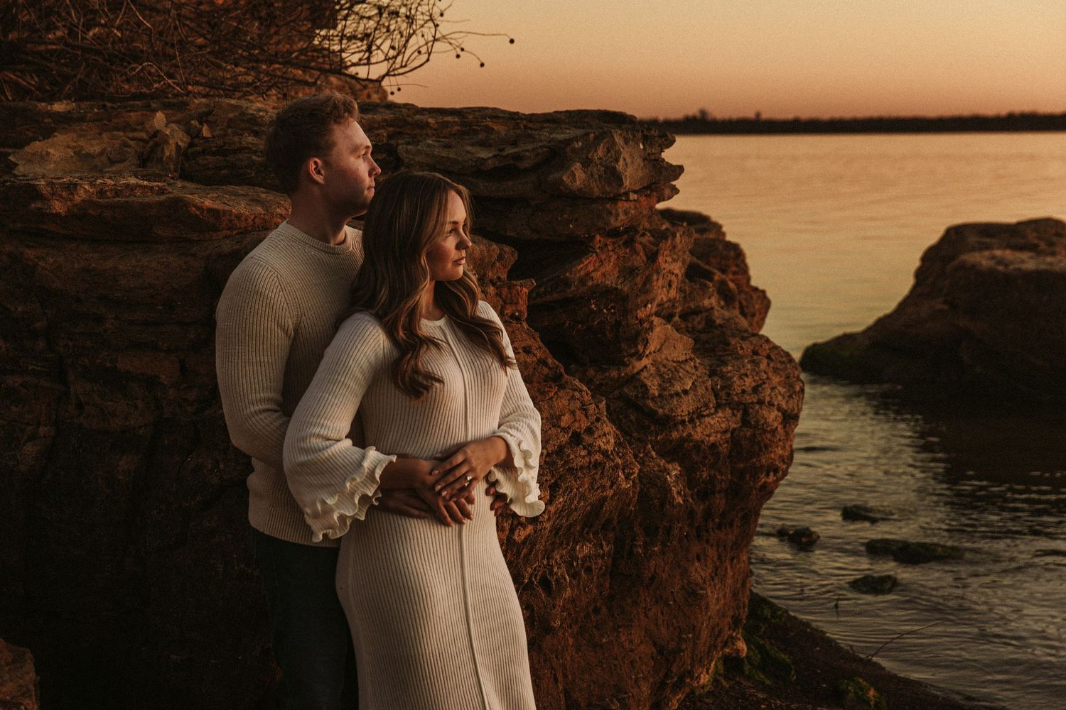 Couple sharing tender moments at sunset along a rocky coastal landscape.
