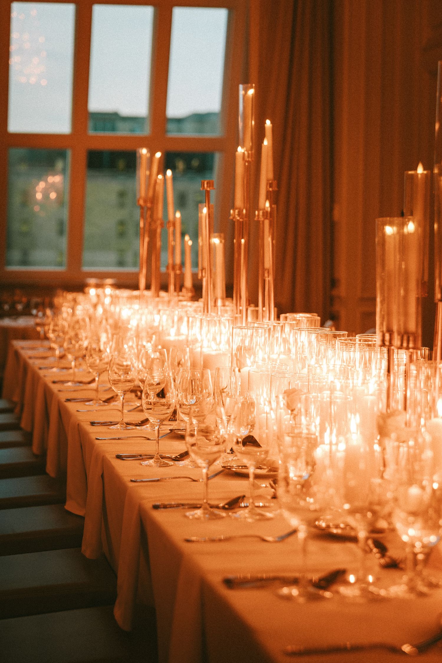 Elegant wedding reception table set with tall candles, crystal glassware, and warm candlelight.