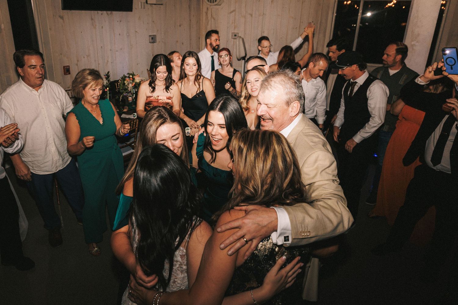 Bride in wedding gown shares a warm group hug with guests on the dance floor during the wedding reception.