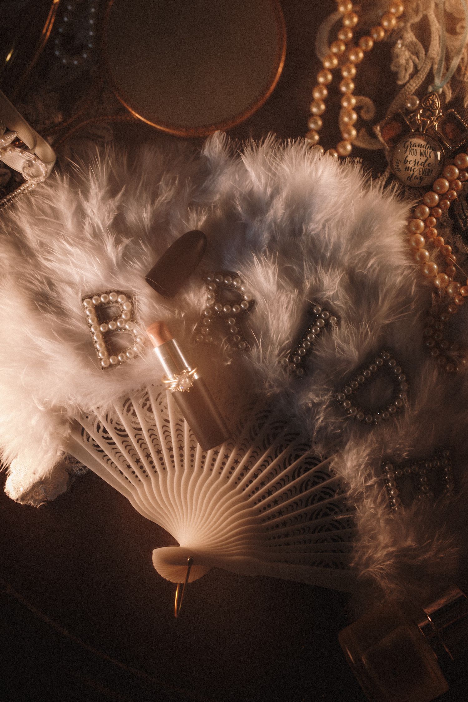 White feather fan with pearl BRIDE letters surrounded by pearls and vintage accessories on dark surface.
