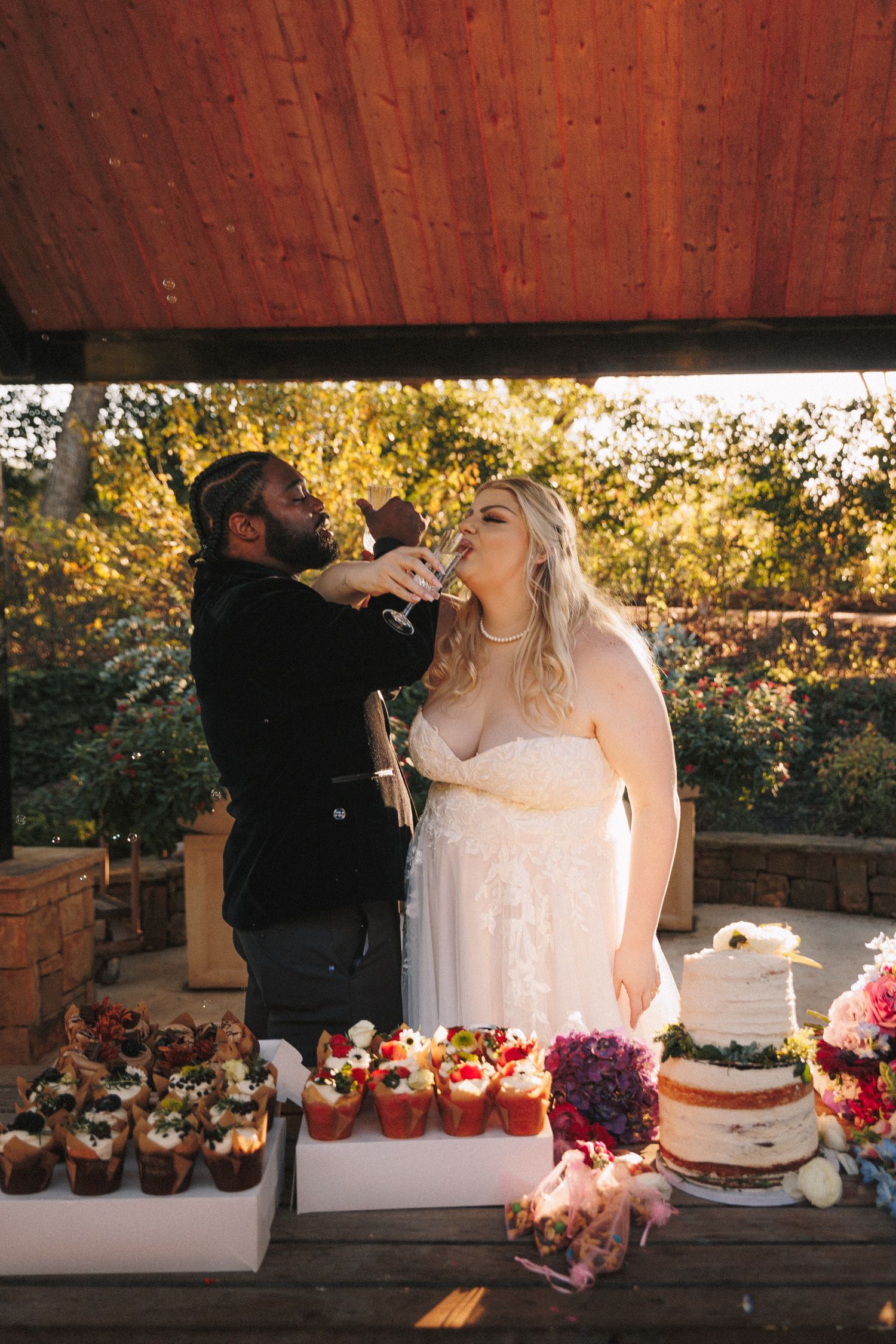Groom feeds bride wedding cake at outdoor autumn reception with floral decorations.