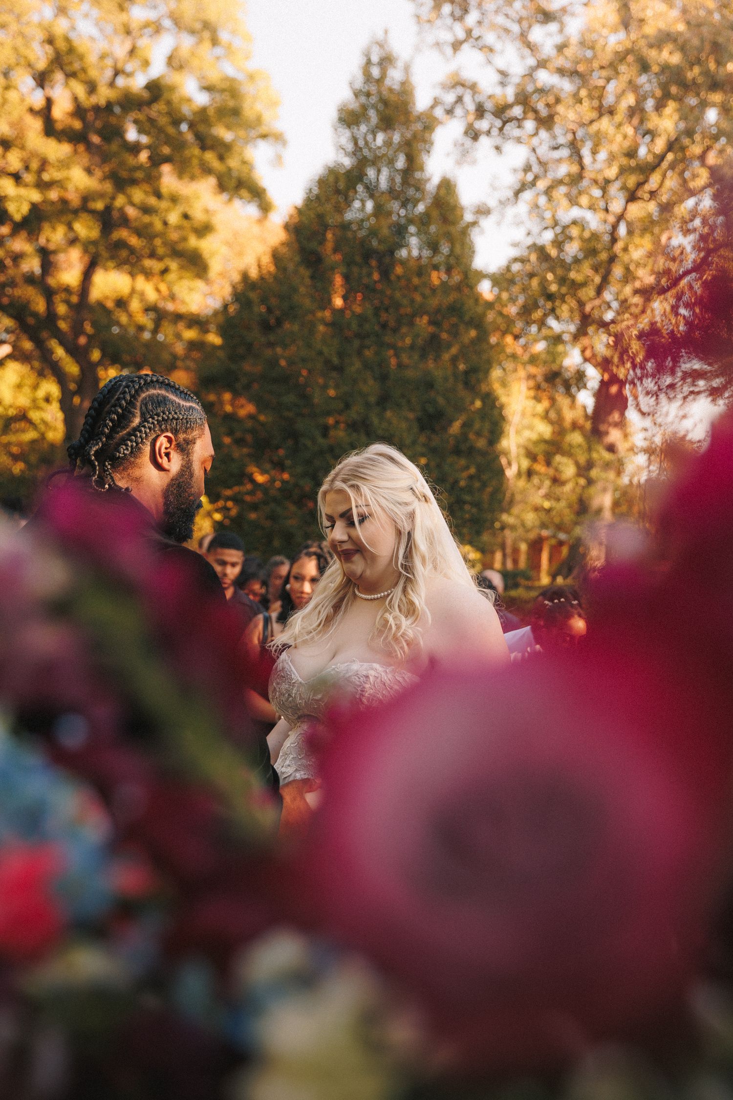 Bride and groom exchange vows at outdoor wedding ceremony framed by vibrant red flowers and autumn foliage.