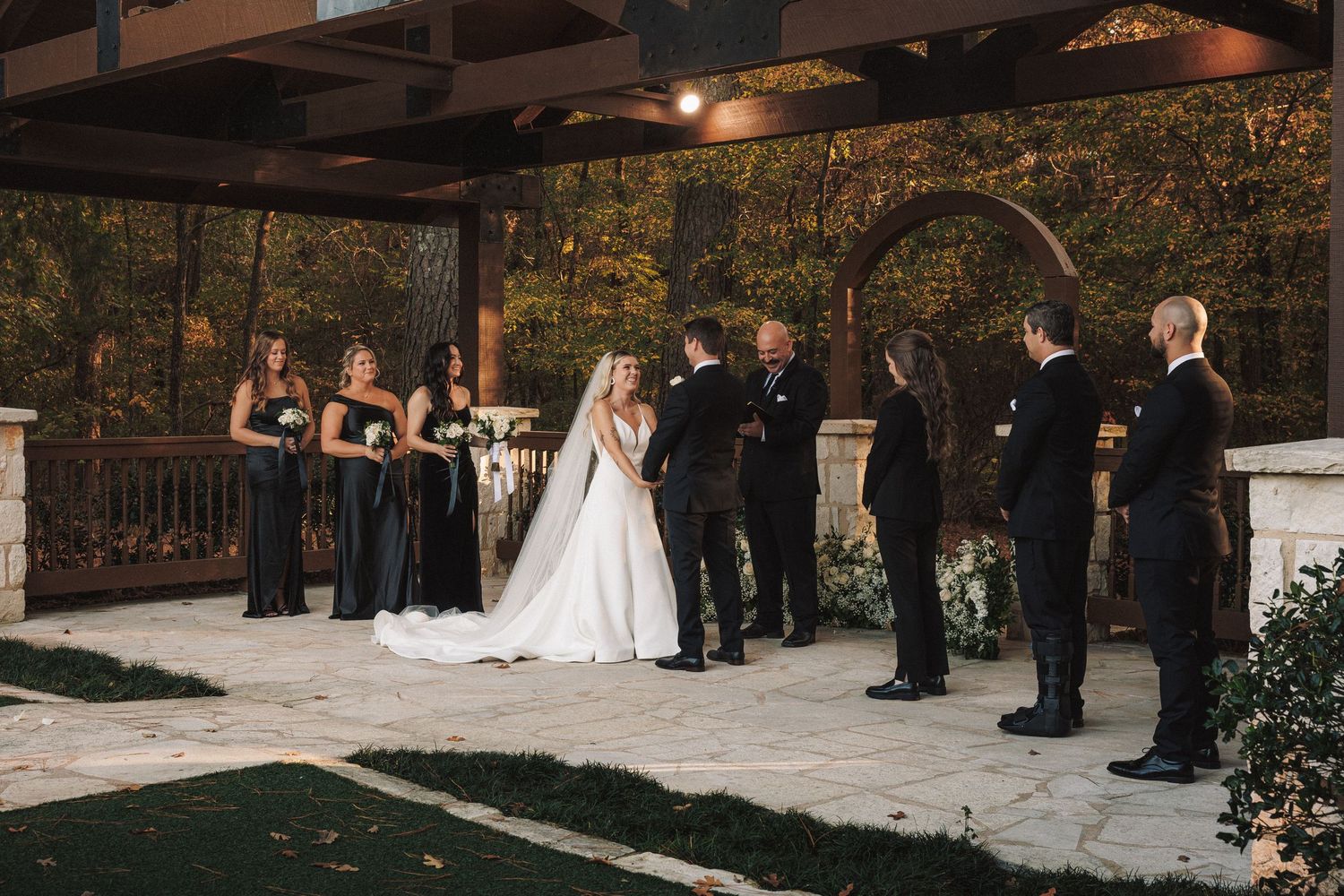 Bride and groom exchange vows under a pergola at an elegant outdoor autumn wedding ceremony.