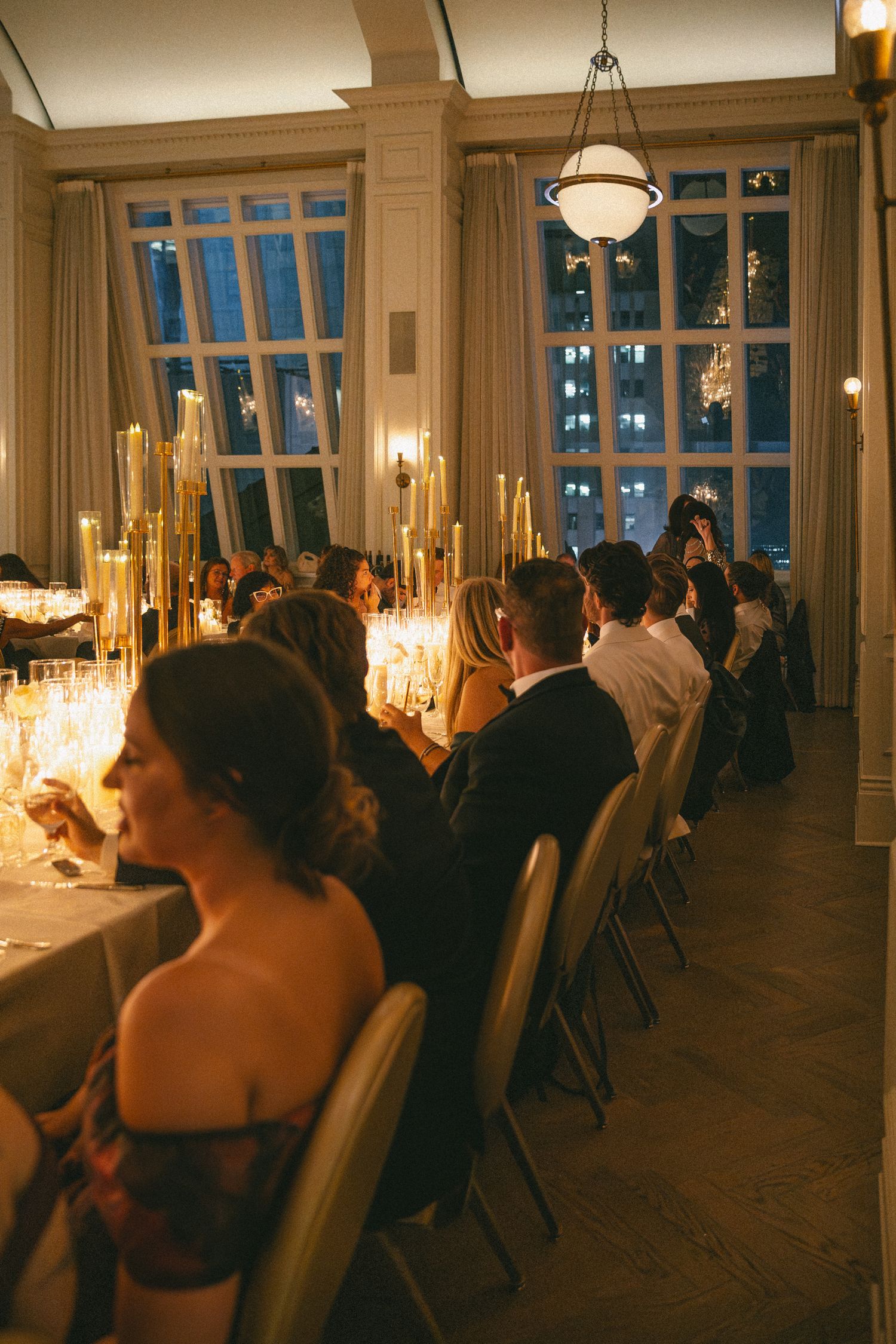 Guests seated at a long candlelit wedding reception dinner table in an elegant ballroom.