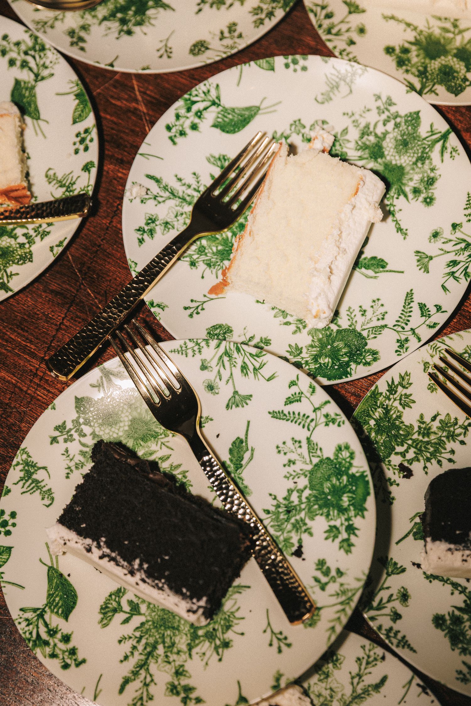 Slices of white and chocolate wedding cake on green botanical floral plates with gold forks.