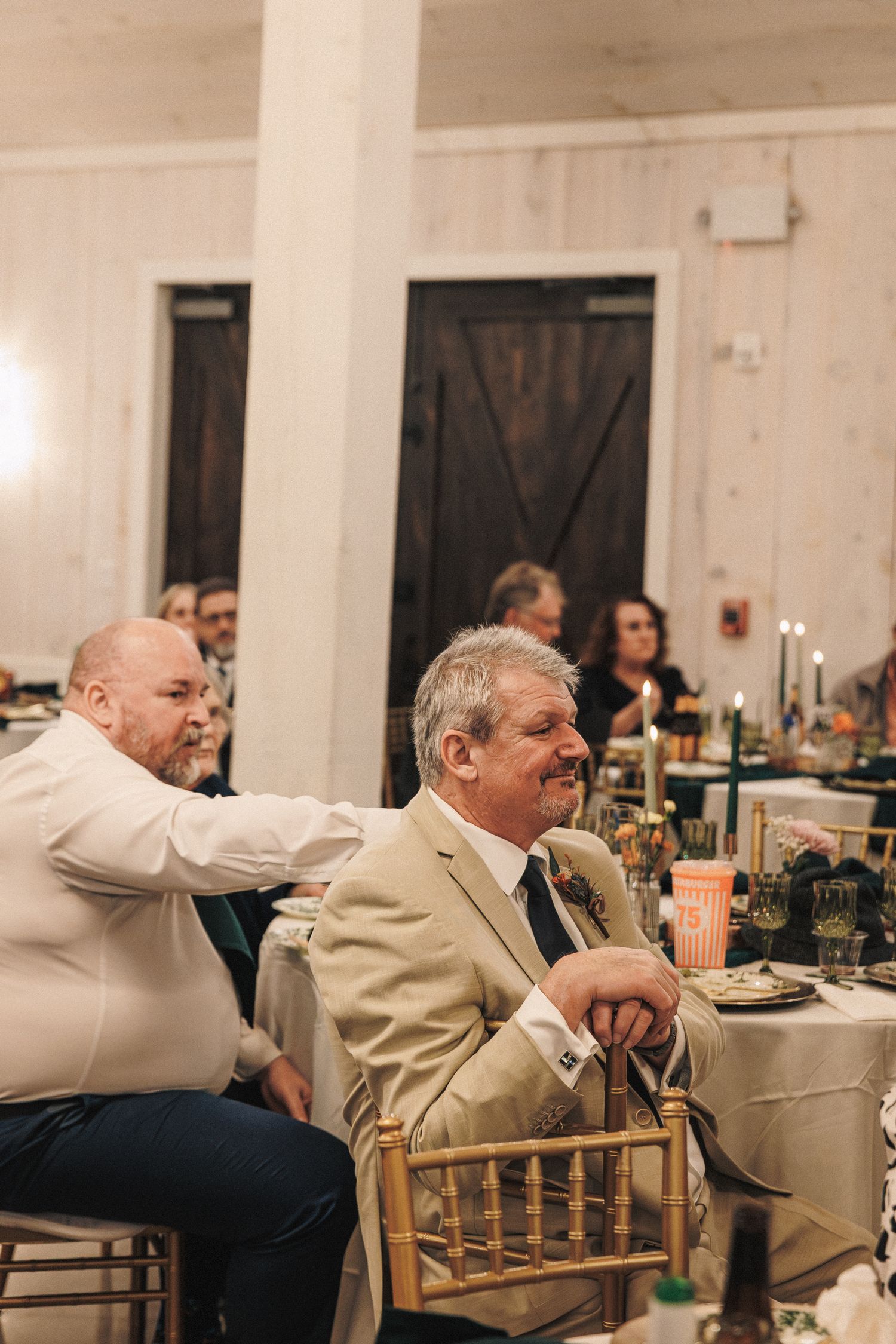 Wedding guests laughing and enjoying reception dinner inside rustic barn venue.